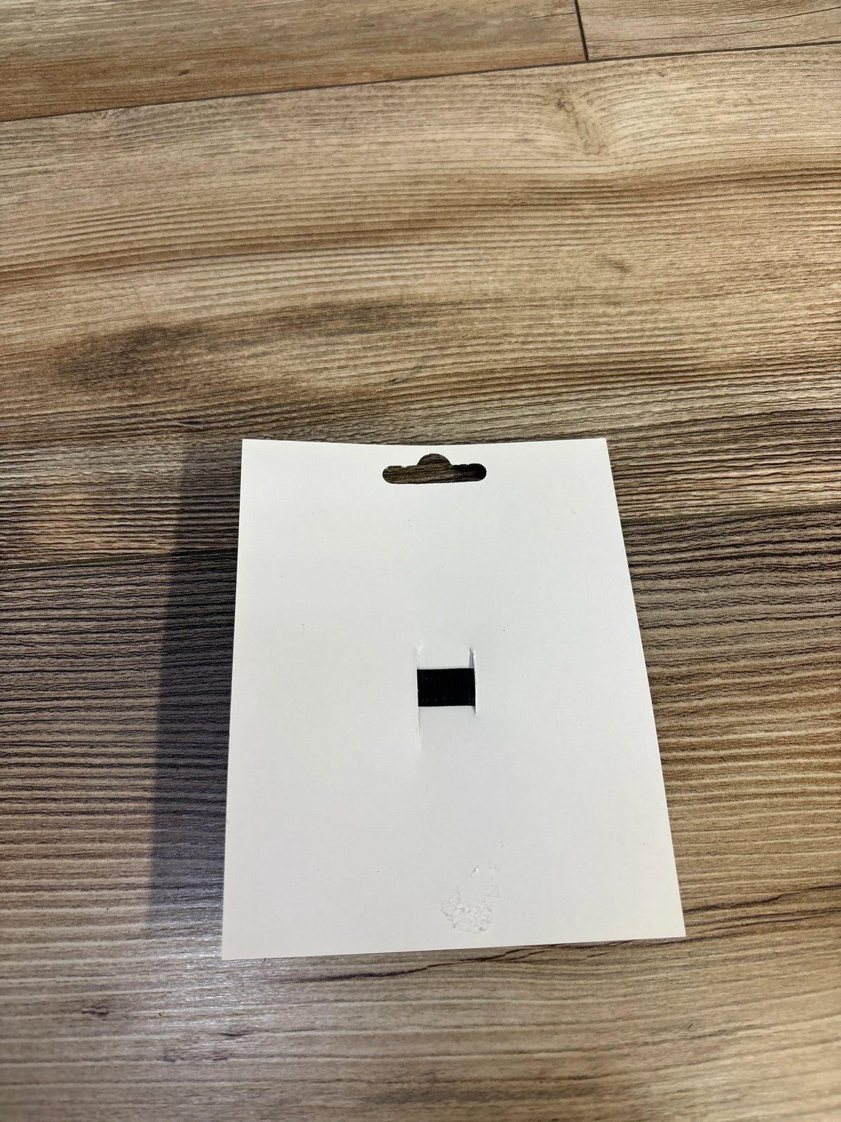 Blank white product tag with hang hole on wood floor, for kids or maternity items