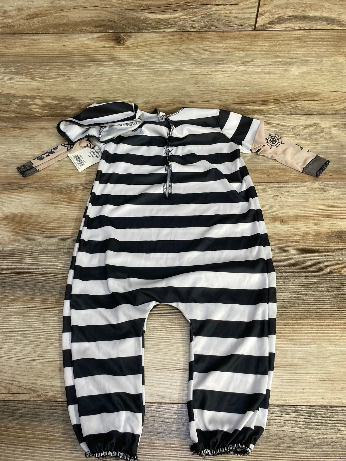Flat lay of Convict Cute 2pc costume set: black and white striped hooded romper with drawstring on wood background