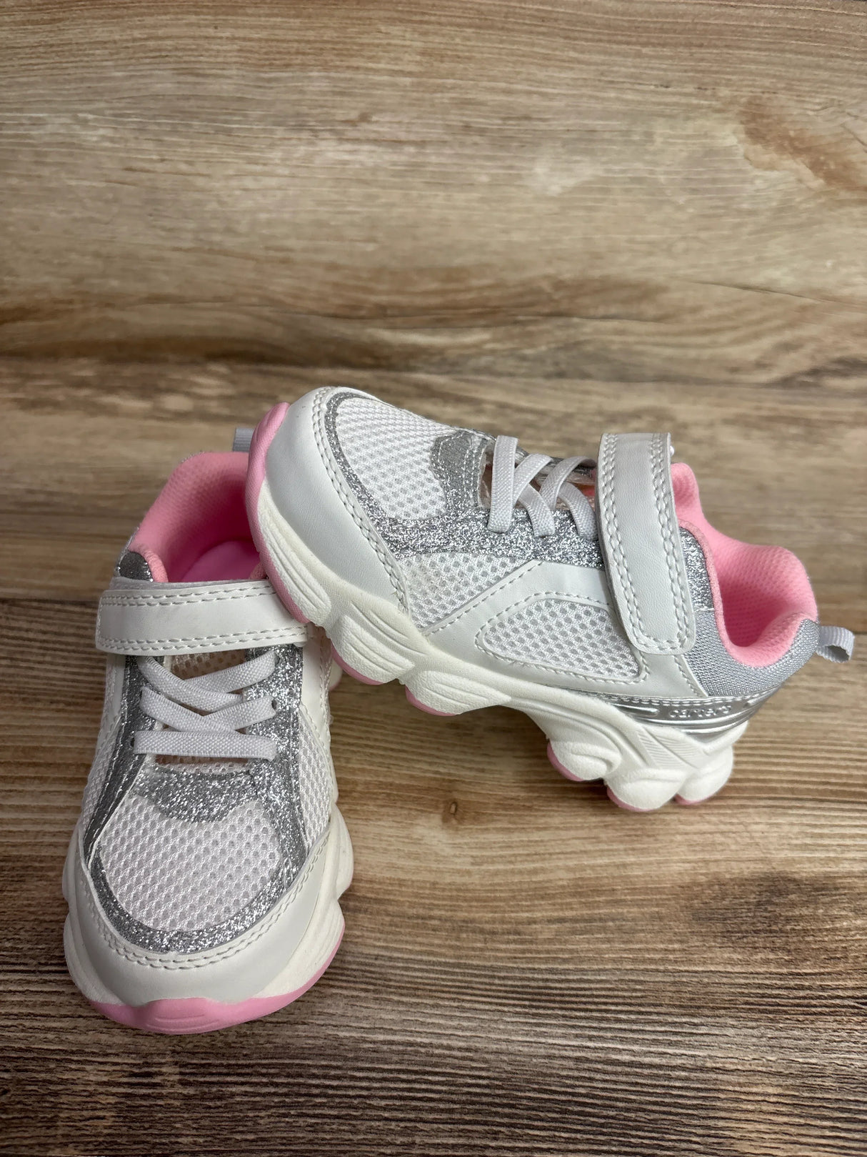 Front and side view of Carter's white toddler athletic sneakers size 9C showing pink lining and silver glitter accents on a wood background