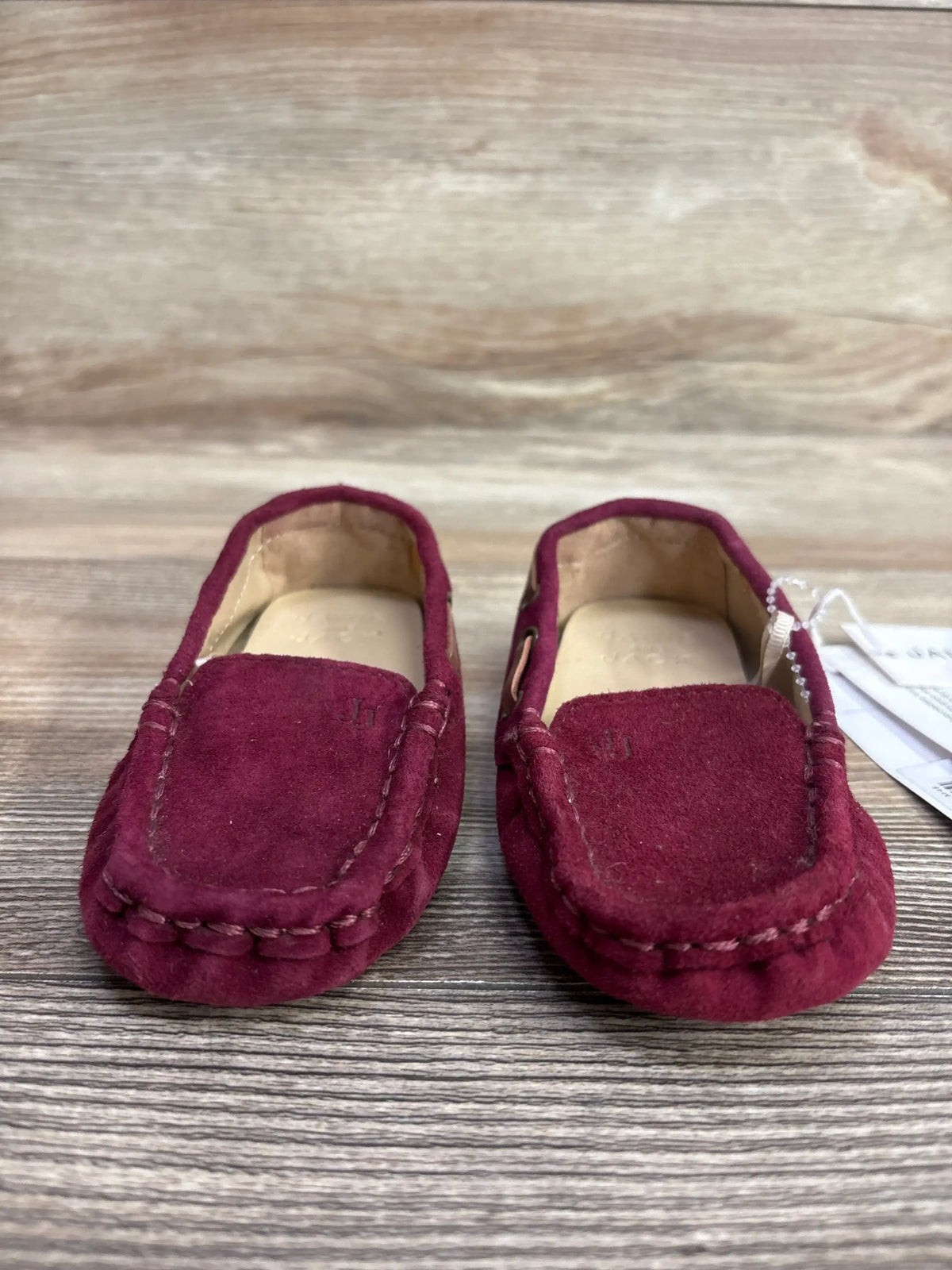 Pair of burgundy suede toddler loafers with stitching detail on wooden surface