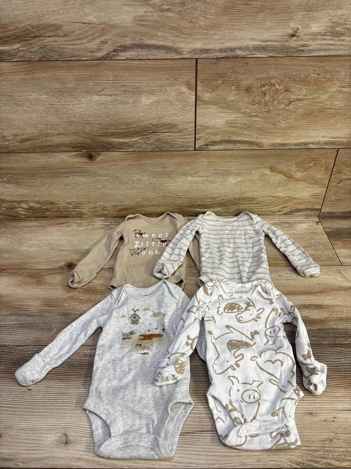 Flat lay of Carter’s 4-pack newborn bodysuits showing grey and cream prints and Sweet little one text on wood background