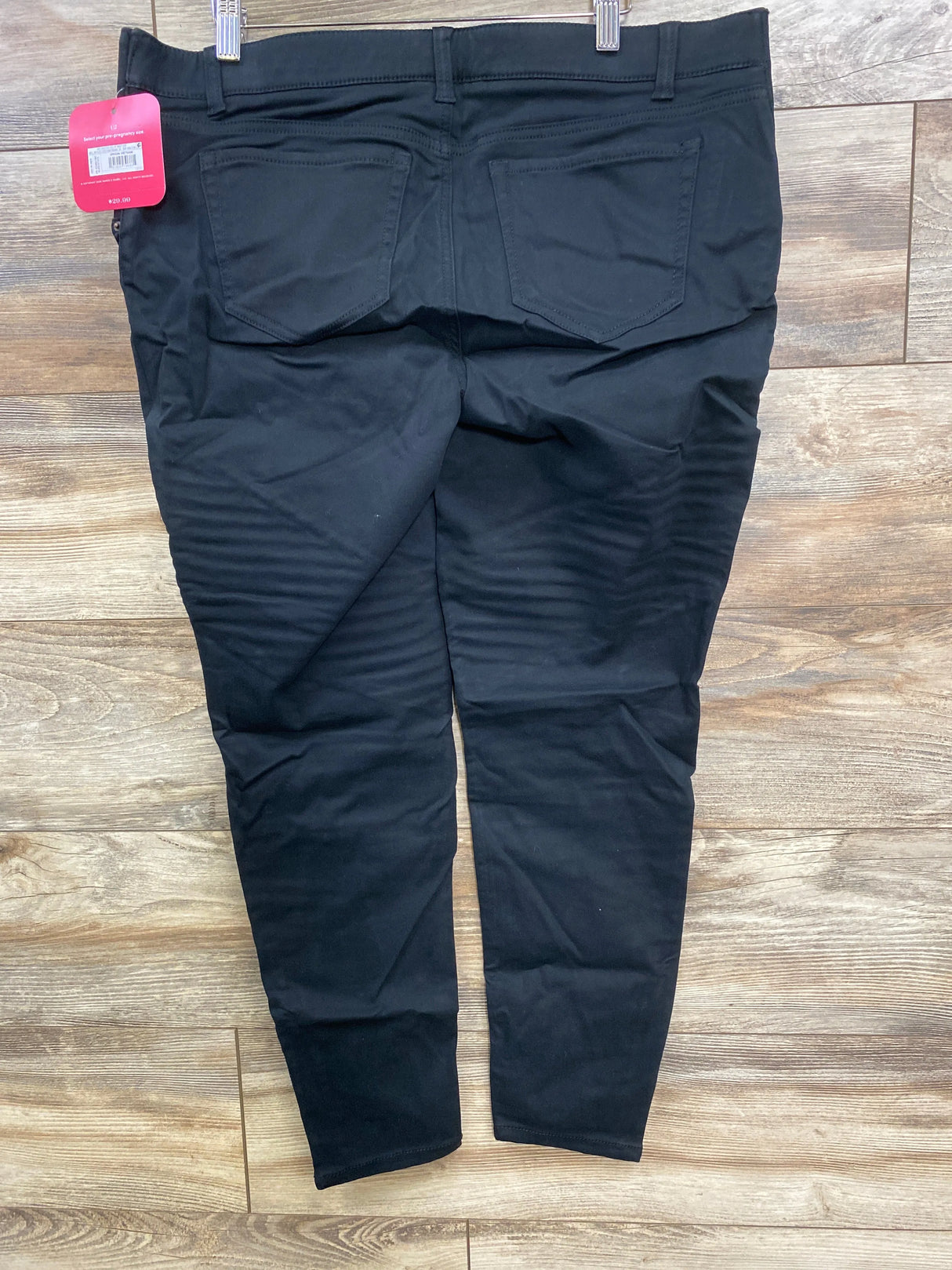 Black maternity pants with back pockets and attached price tag, displayed on wooden floor