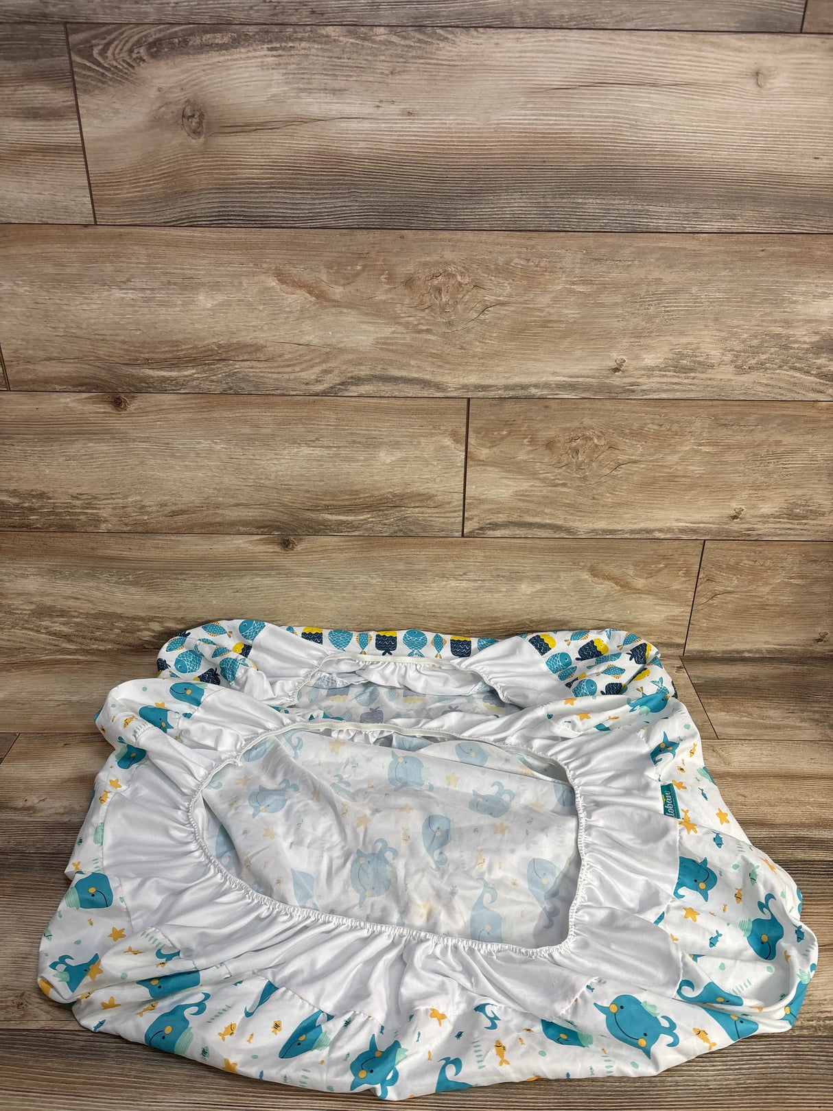 Blue and white fitted crib sheet with whale and fish patterns on wooden surface