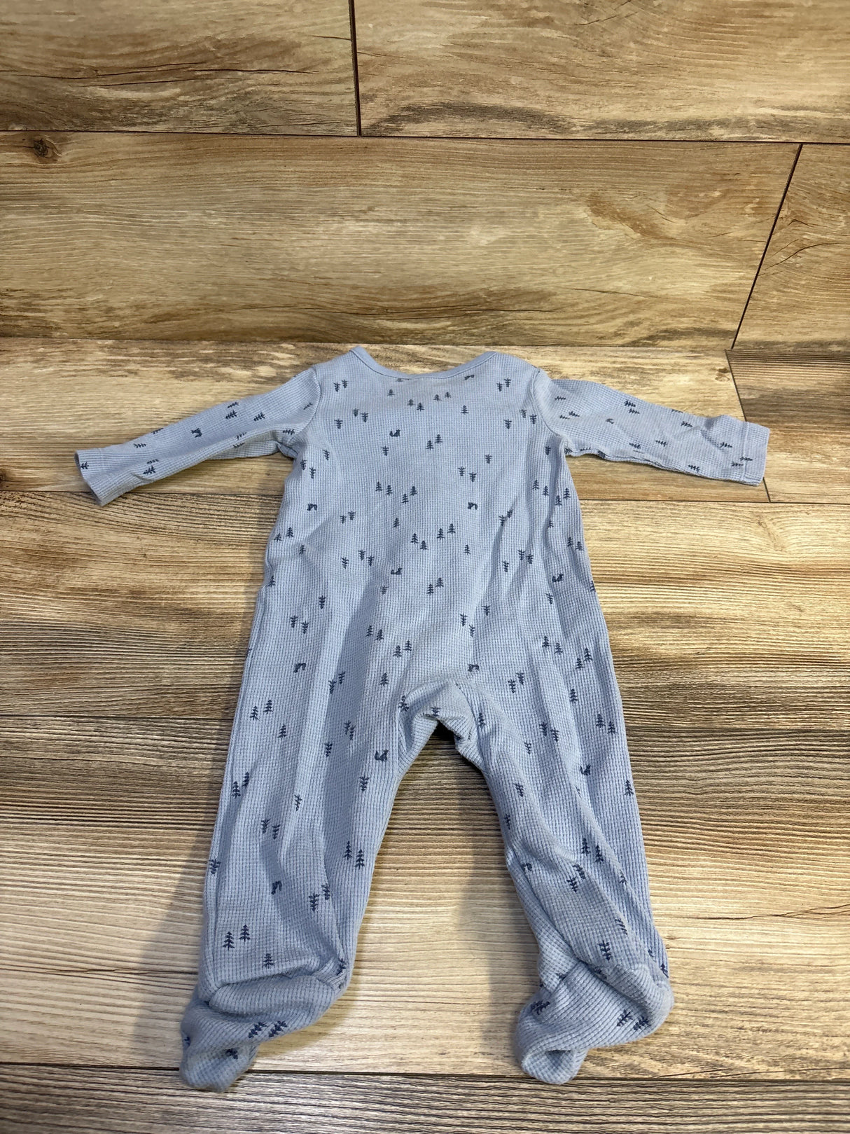 Flat lay of Just One You blue waffle-knit footed sleeper with small tree print on light wood background