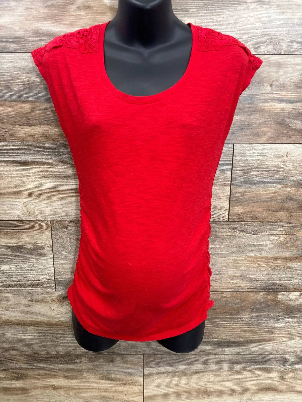 Red maternity shirt with lace shoulder detail on mannequin, wooden background