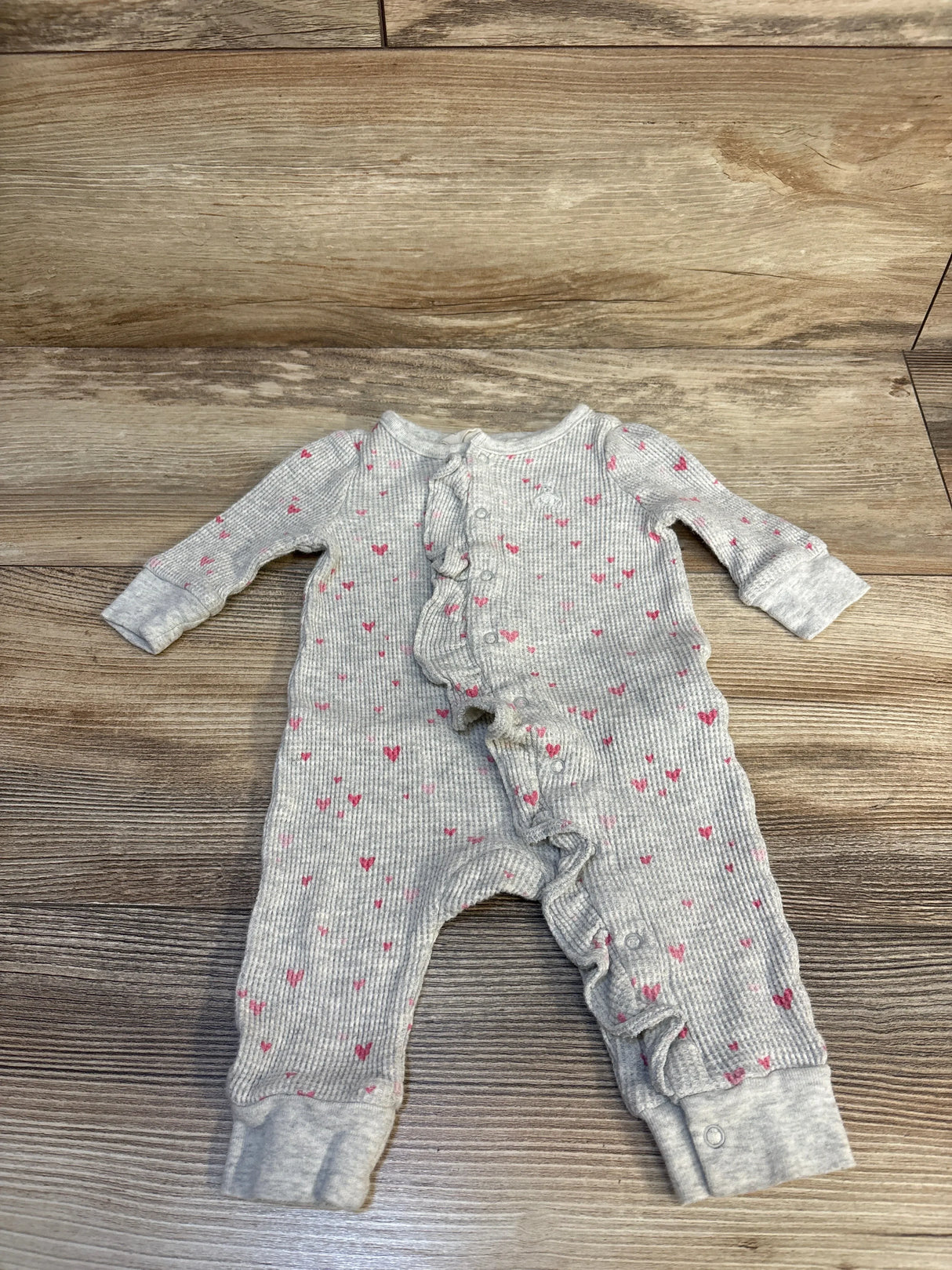 Grey ribbed baby romper with pink heart pattern and ruffle detail on wood background