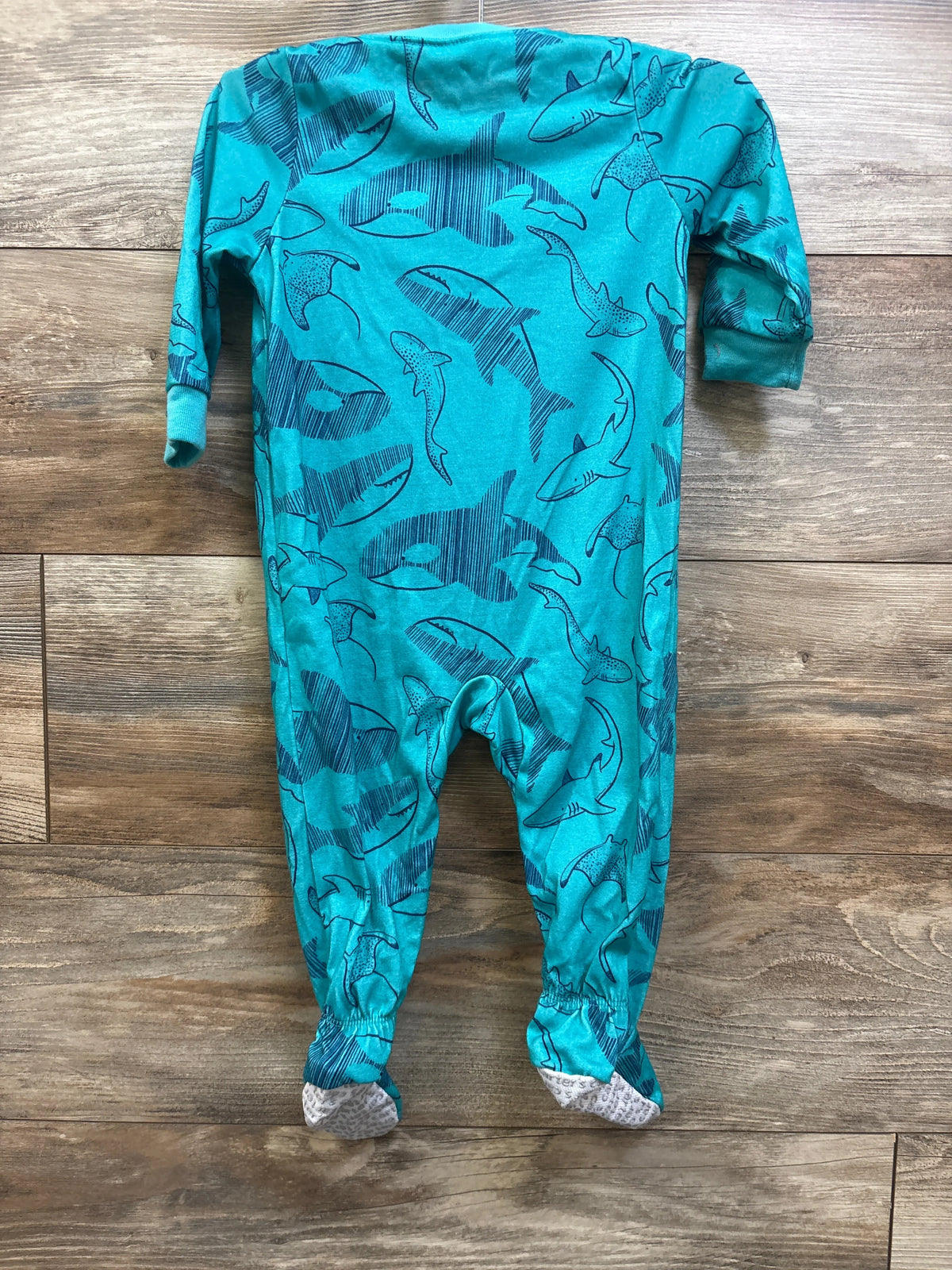 Front view of Just One You teal sleeper, size 12 months, showcasing an all-over shark print and footed legs on a wood floor