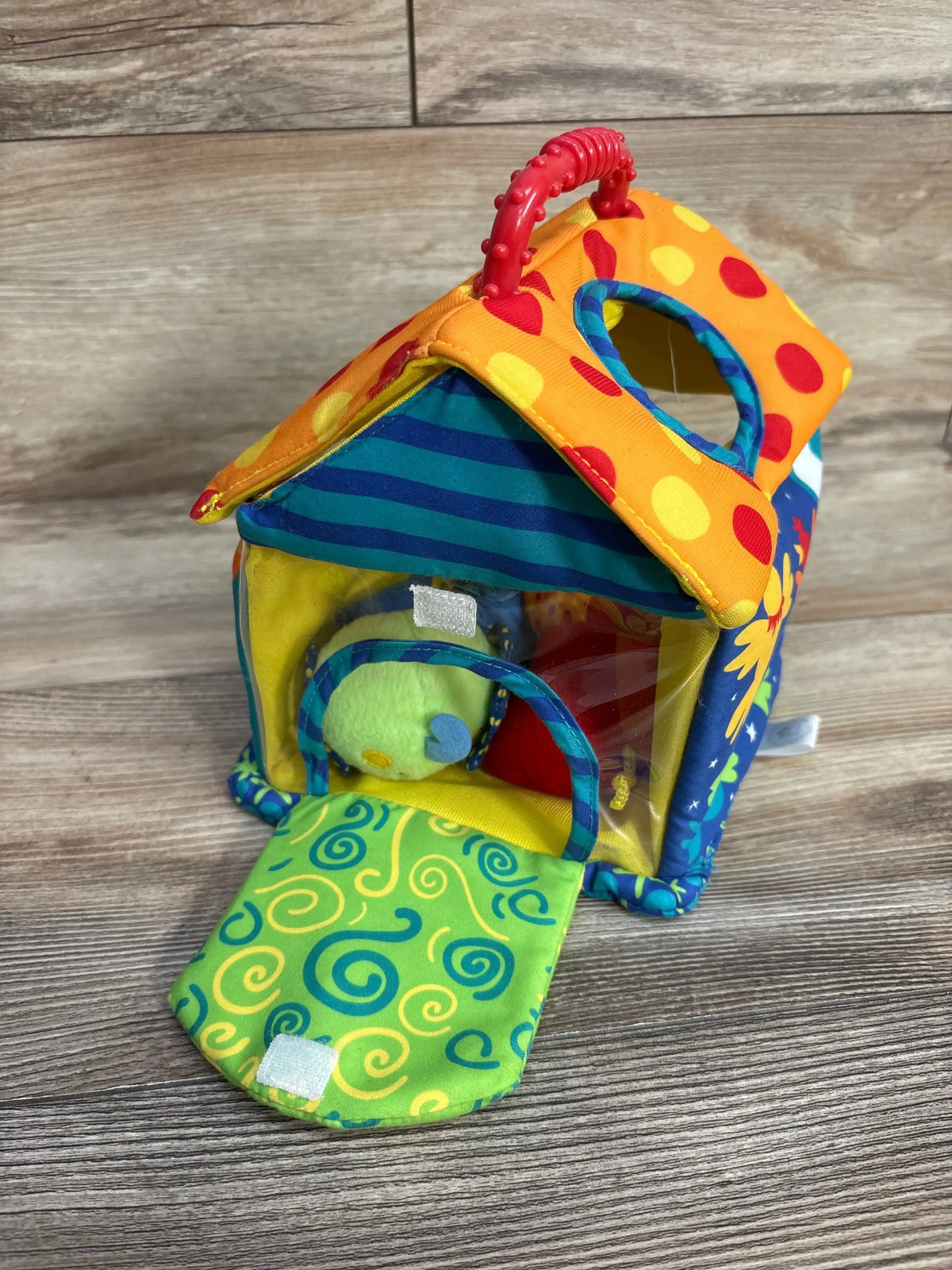 Three-quarter view of Manhattan Toys Put & Peek Birdhouse with polka-dot roof, red handle, open door revealing plush bird