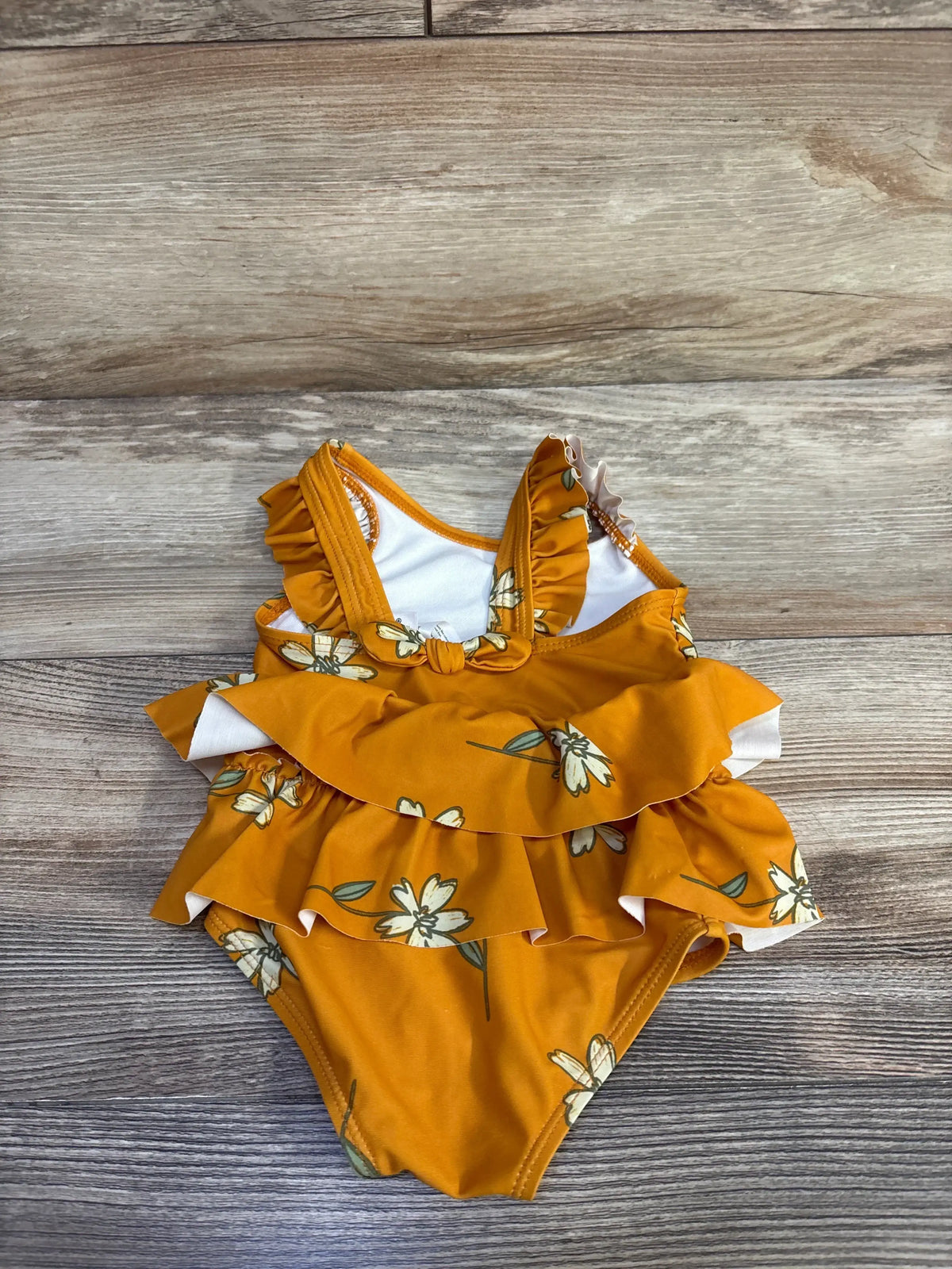 Top-down view of orange Carter's 1-piece floral swimsuit with layered front ruffles and knotted chest on wood background