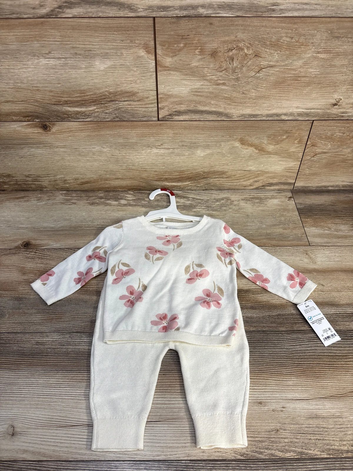 Front view of ivory two-piece knit sweatshirt and pants set showcasing pink floral pattern on a wooden background