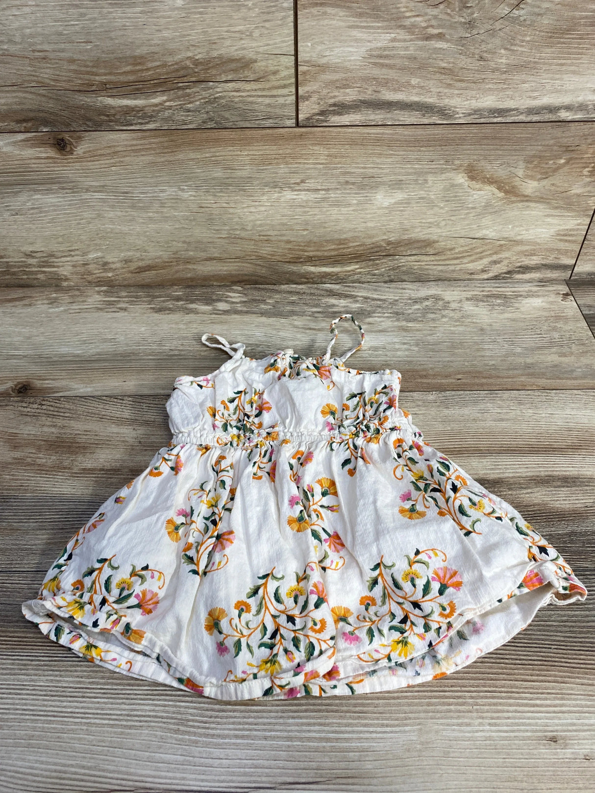 Flat lay of Old Navy toddler cream floral dress showcasing ruffle trim and smocked bodice with wood plank background