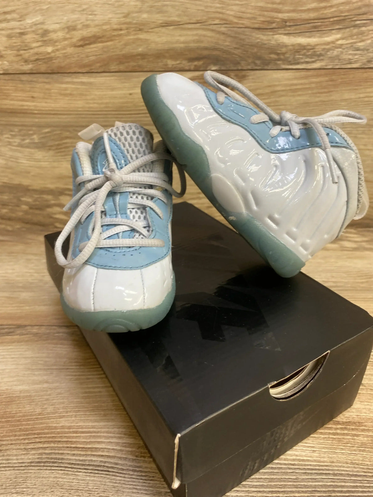 Angled view of Nike Little Posite One toddler sneaker with glossy white and blue upper and translucent sole on shoebox