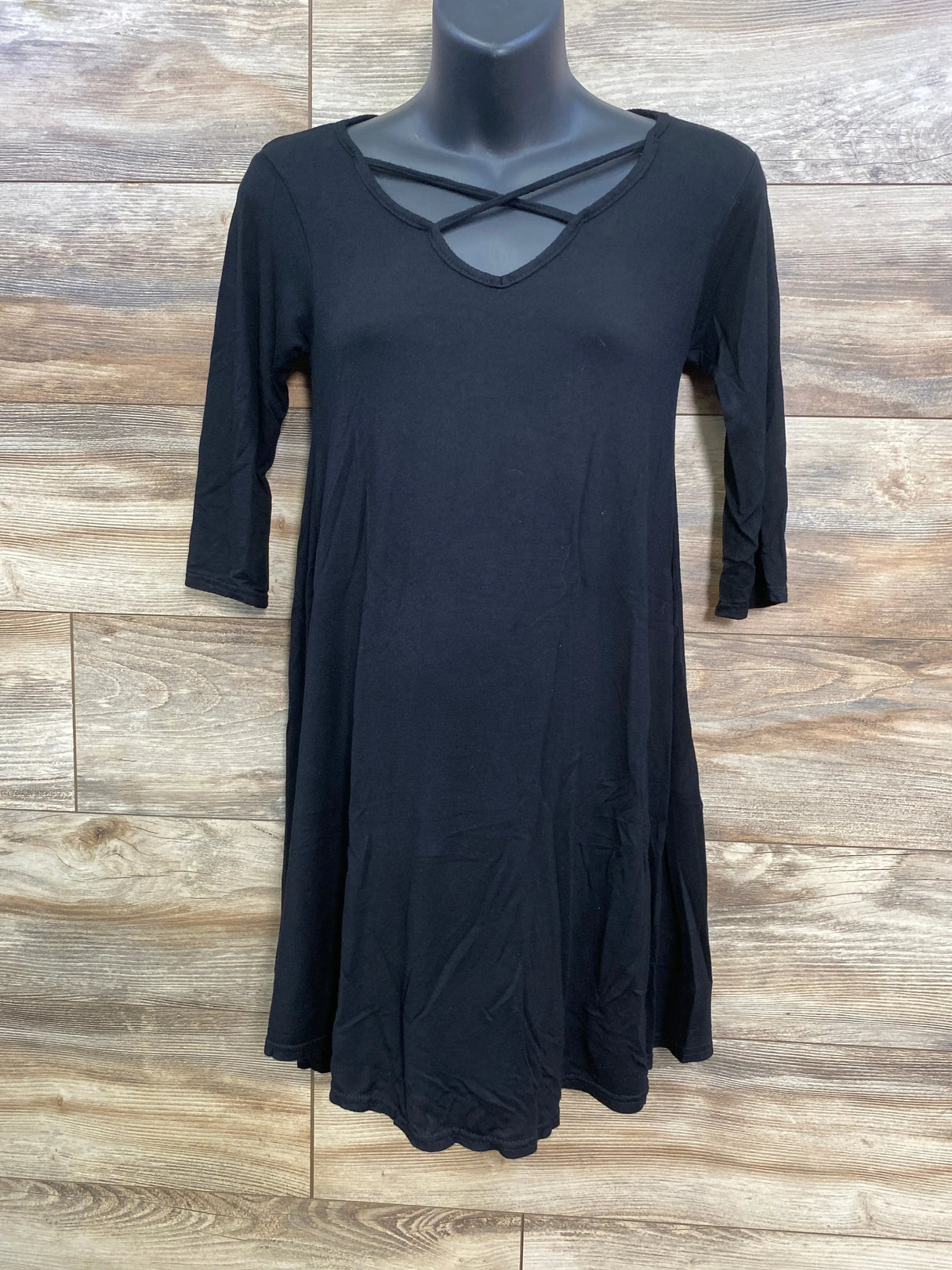Front of black maternity swing top with three quarter sleeves and crossed strap V neck on mannequin wood background