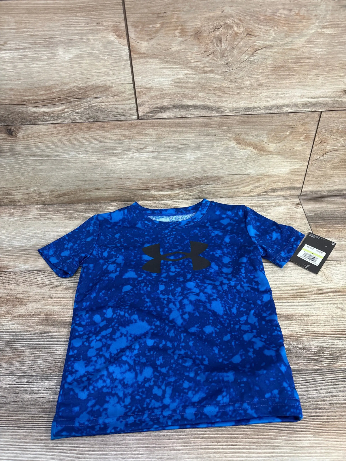 Front view of boys’ Under Armour blue mottled short-sleeve active shirt showing black UA logo on wood floor
