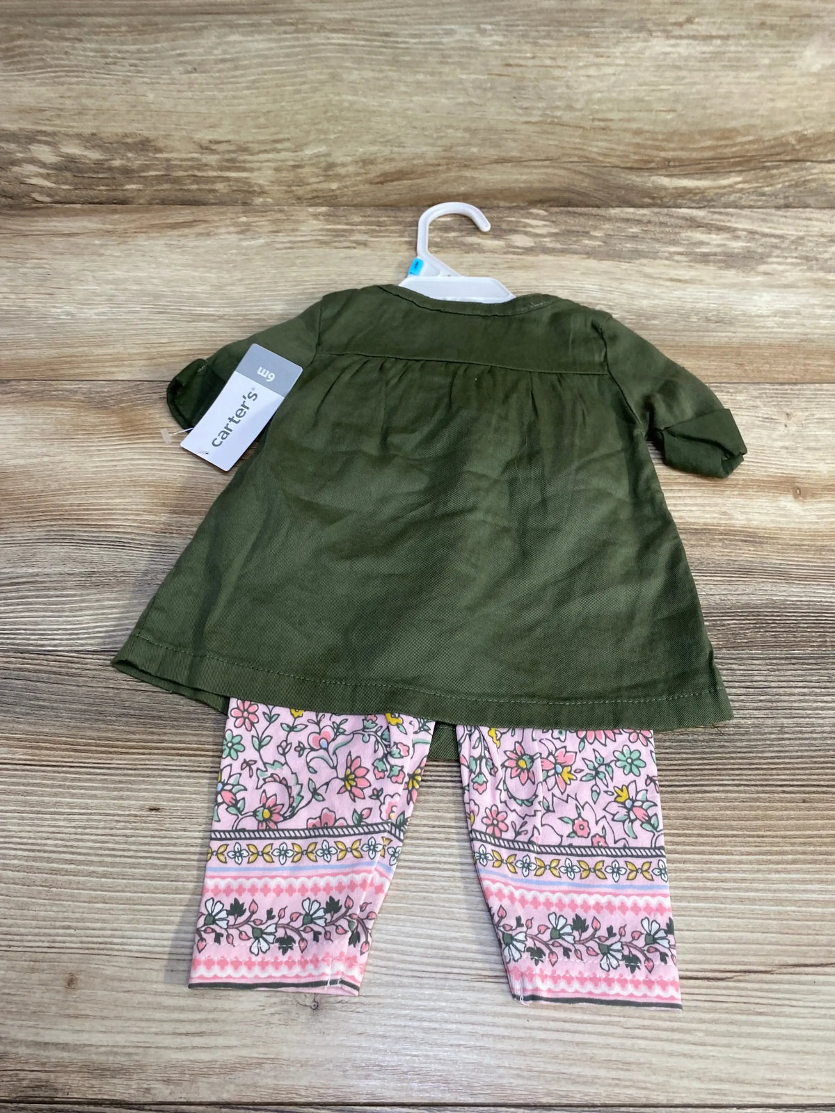 Back view of Carter’s green top and floral leggings set in size 6 months on a hanger over a wood surface