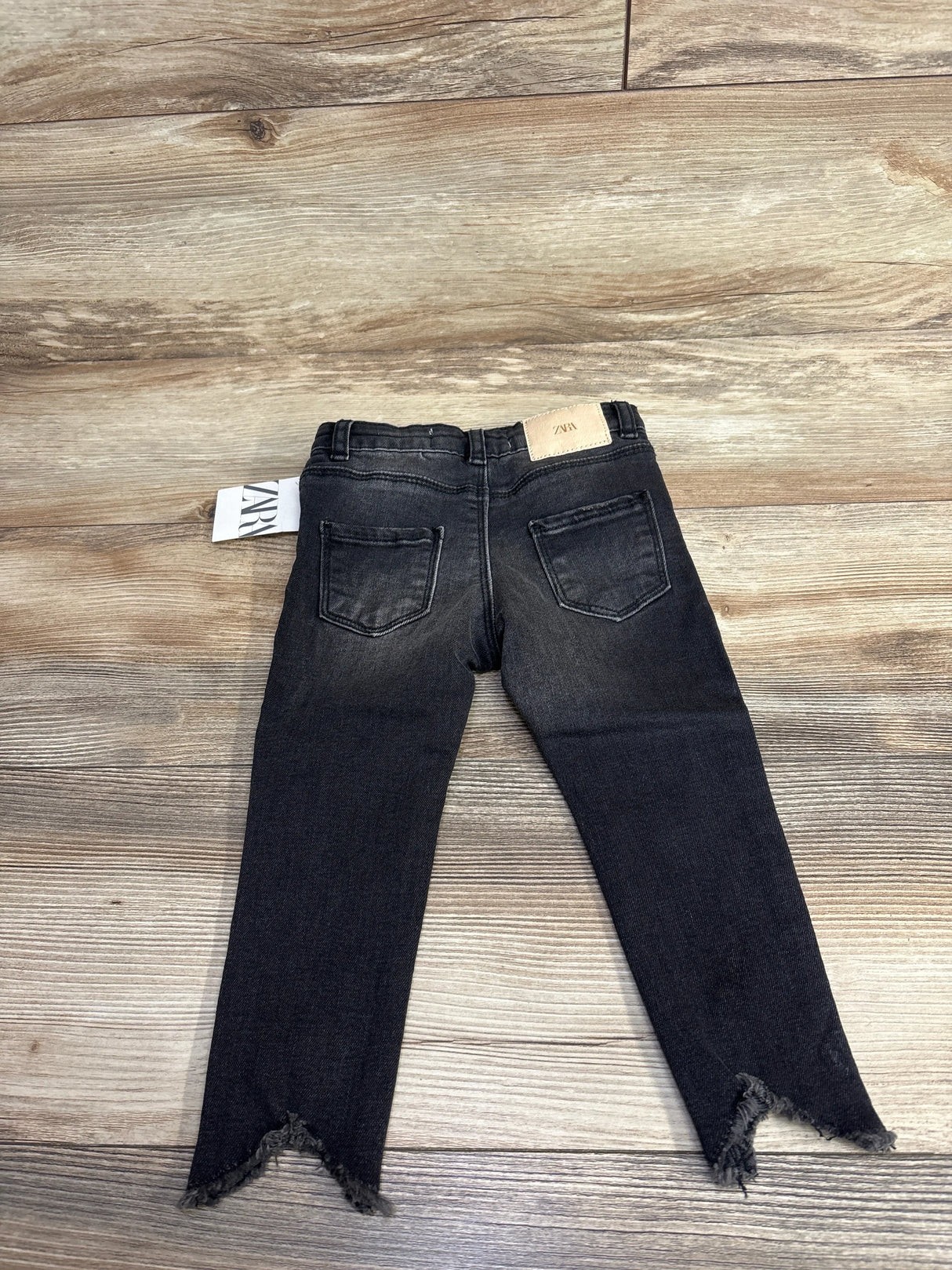 Back view of black Zara toddler jeans with frayed hems on wood floor, children's clothing