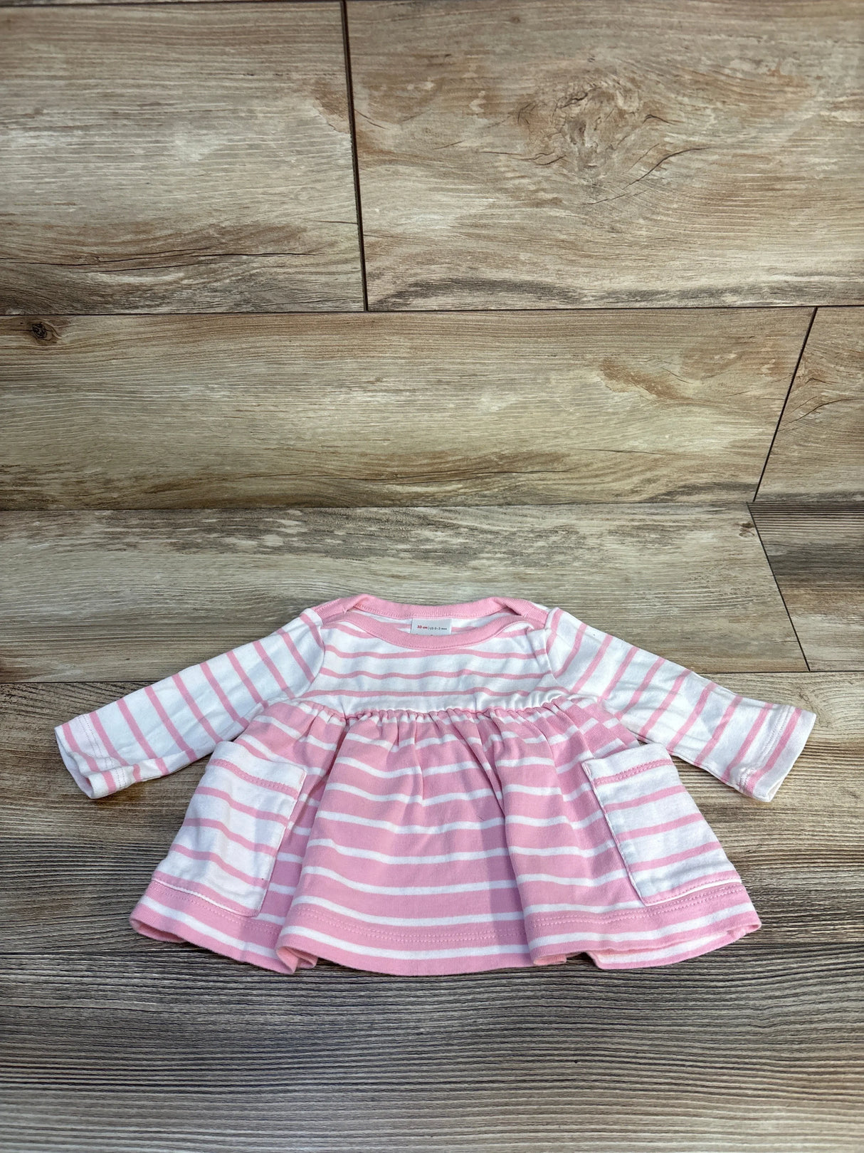Pink and white striped long sleeve baby dress with pockets on wood floor