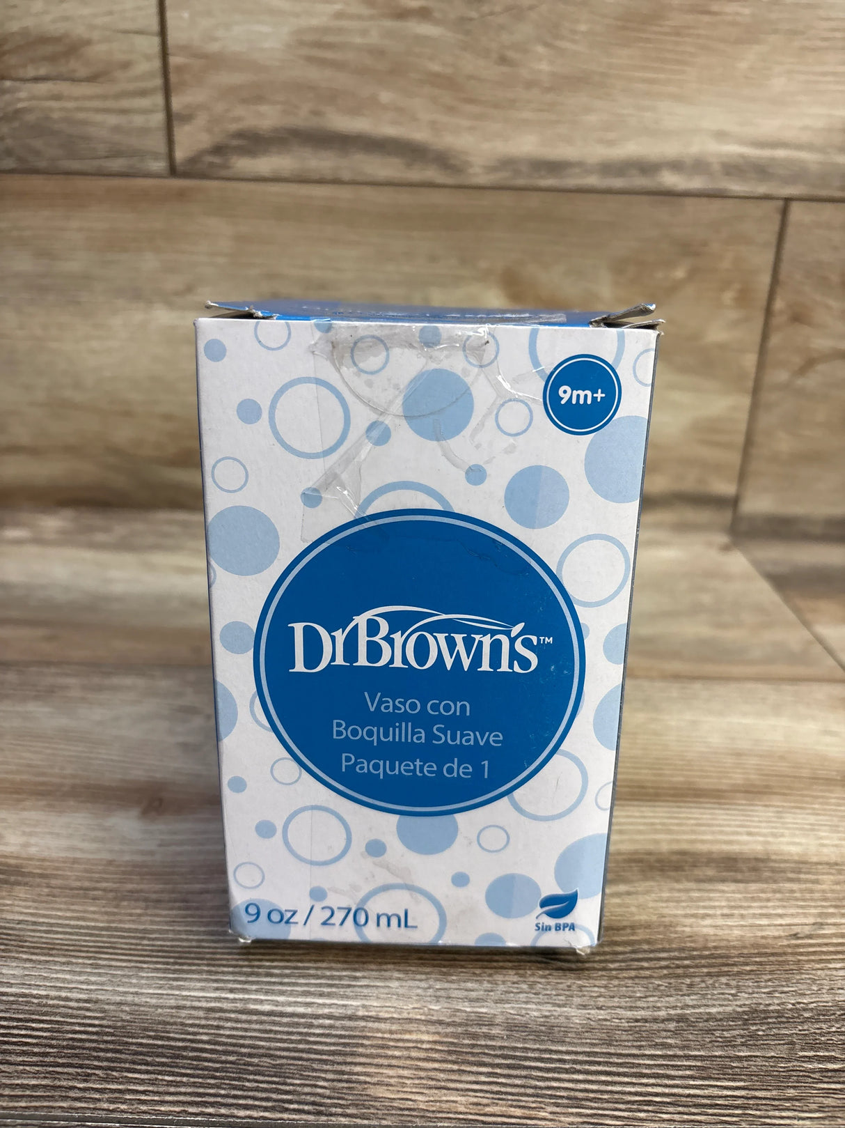 Front view of Dr. Brown’s 9 oz soft-spout toddler cup box showcasing logo, Spanish product text and 9m+ age circle on wood surface