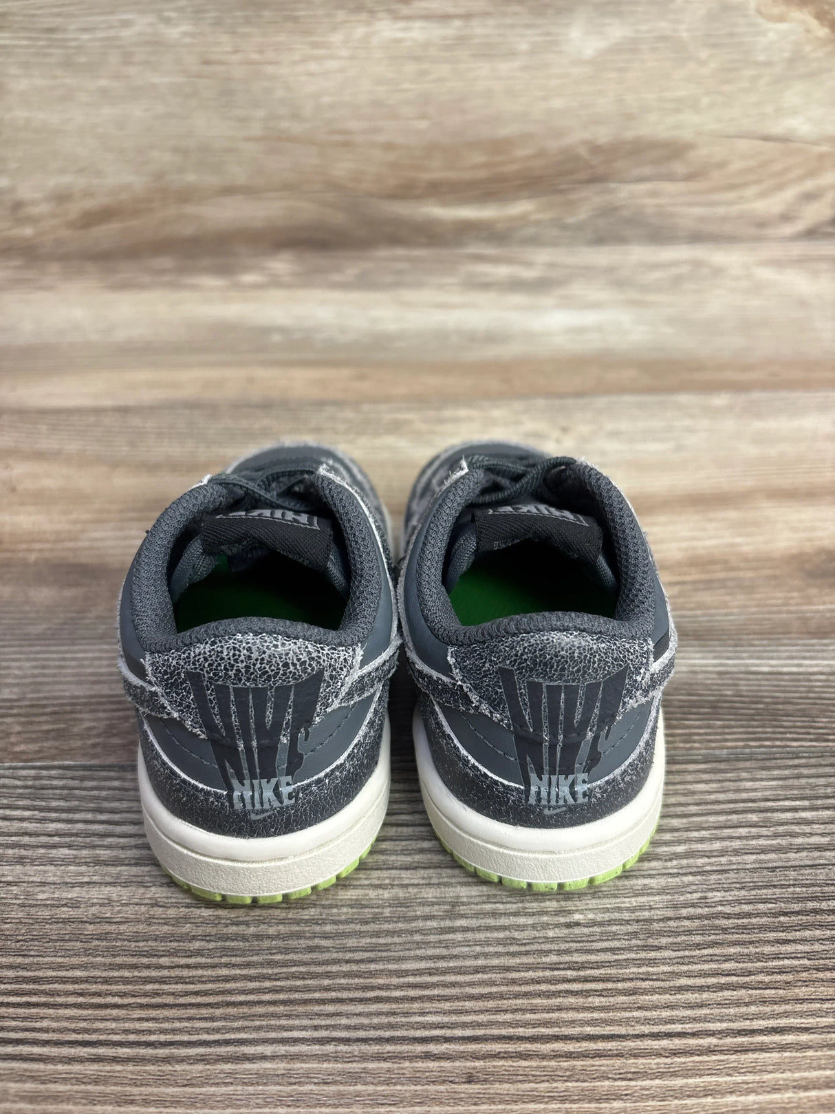 Nike toddler sneakers with gray mesh, white soles, and lime green accents on wood floor