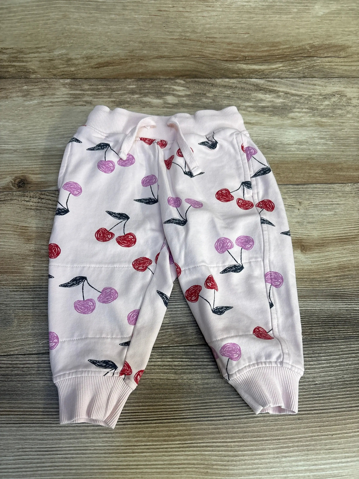 Pink baby jogger pants with red and purple cherry print on wood background