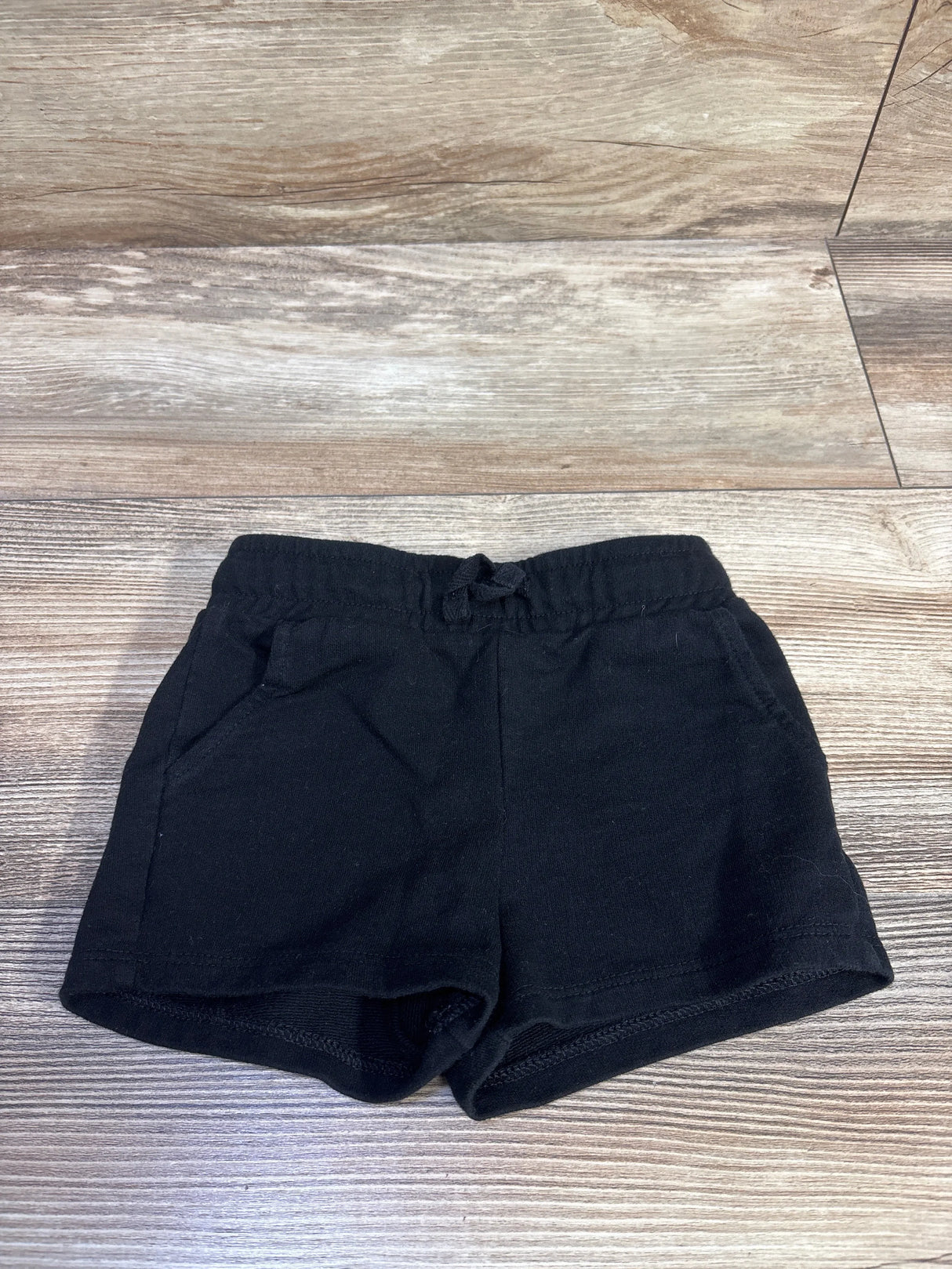 Flat lay front view of toddler black Cat & Jack knit shorts showcasing elastic waistband with tie and side pockets on a light wood floor