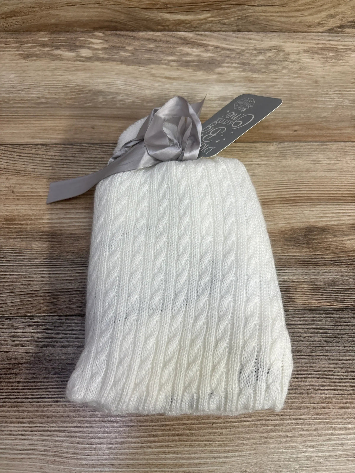 White cable knit baby blanket with gray ribbon on wood background