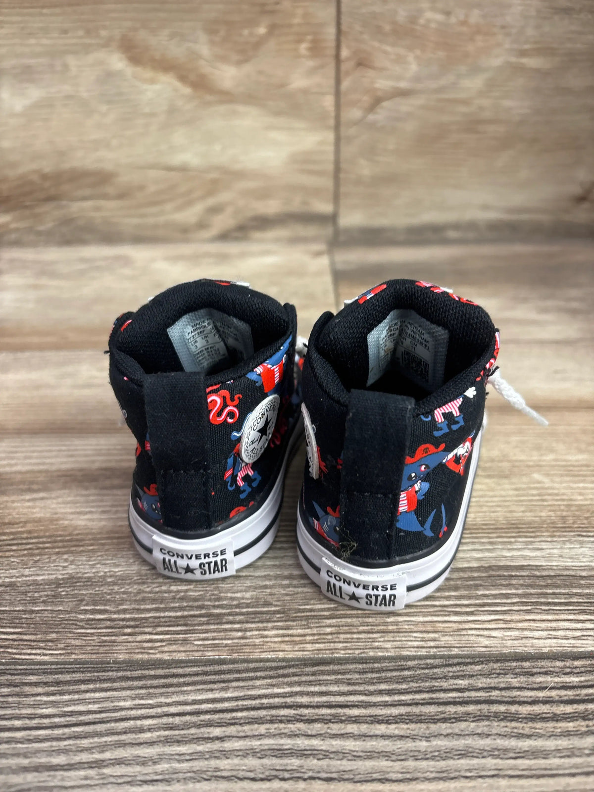Rear view of Converse Chuck All Star Street Mid Sneakers in black showcasing colorful character print and white rubber soles on a wood floor