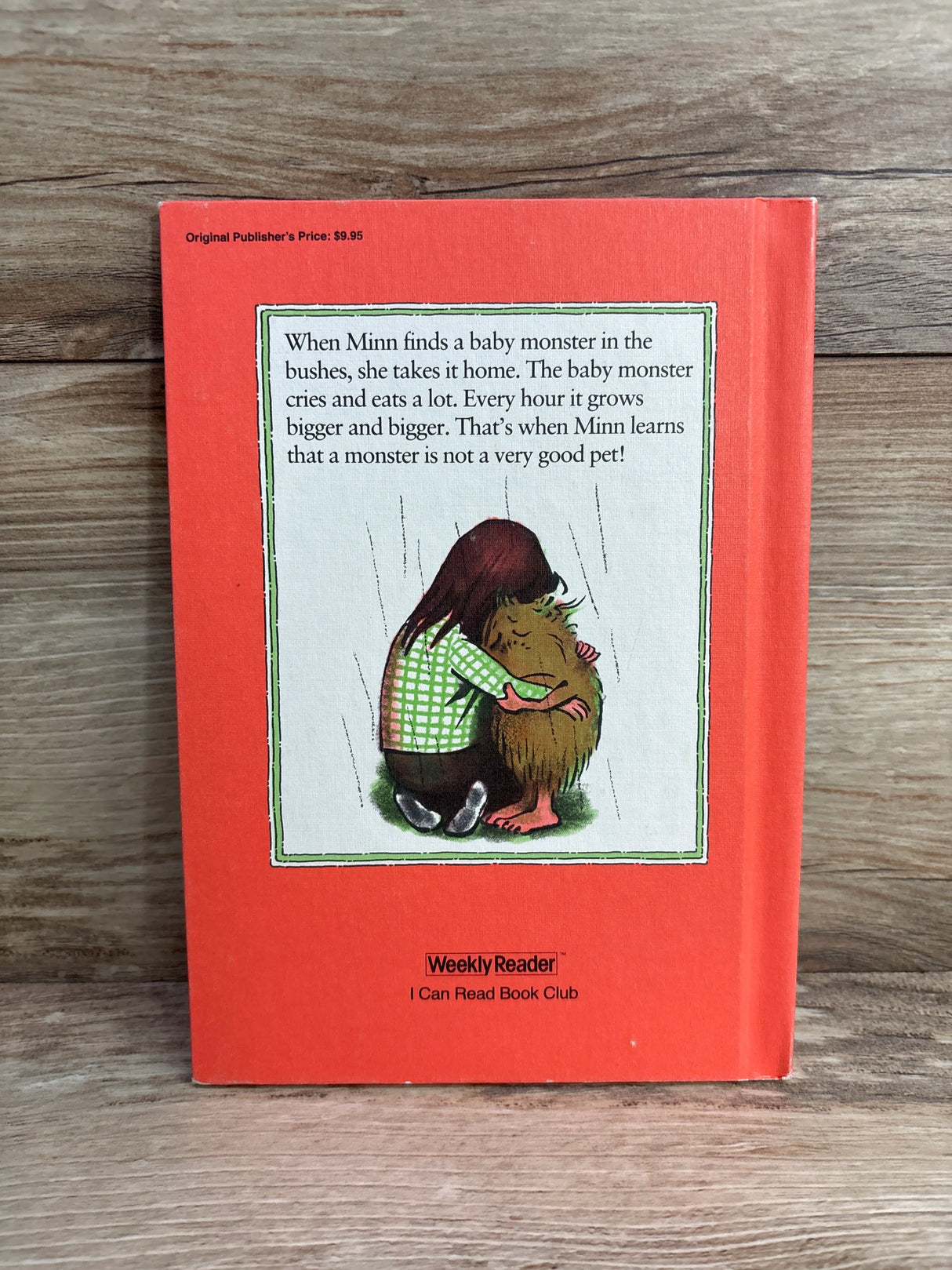 Back cover of a children's book with illustration of a girl hugging a baby monster and summary text on orange background