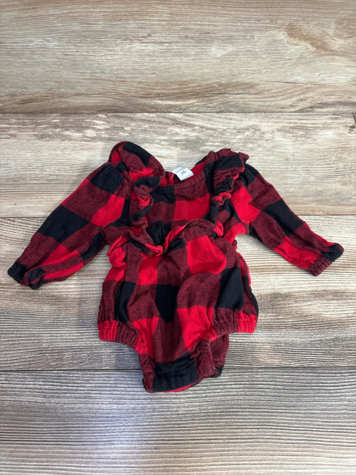 Red and black buffalo plaid long-sleeve baby romper with ruffles on rustic wood background