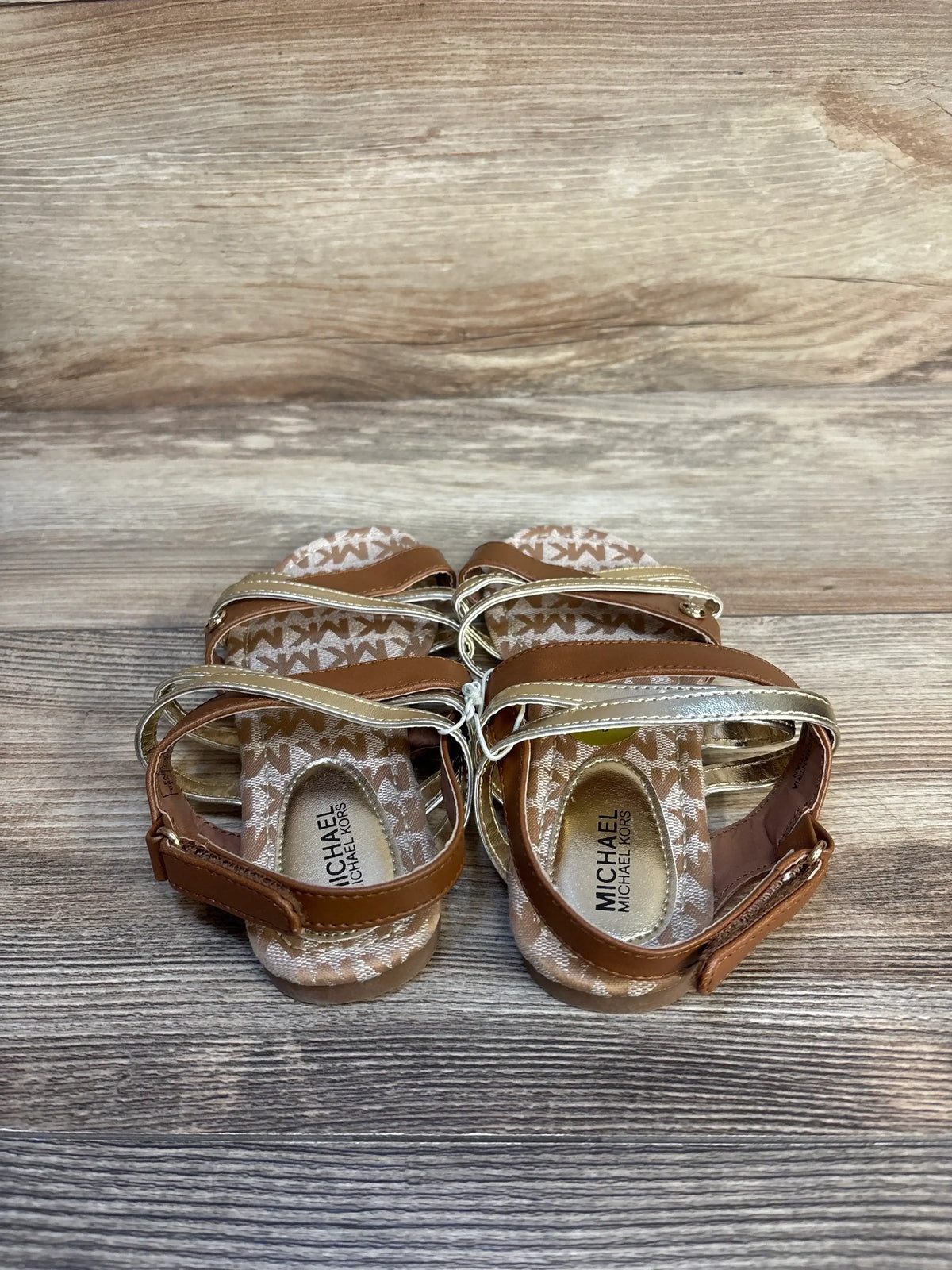Brown and gold Michael Kors toddler sandals with monogram pattern on wooden background