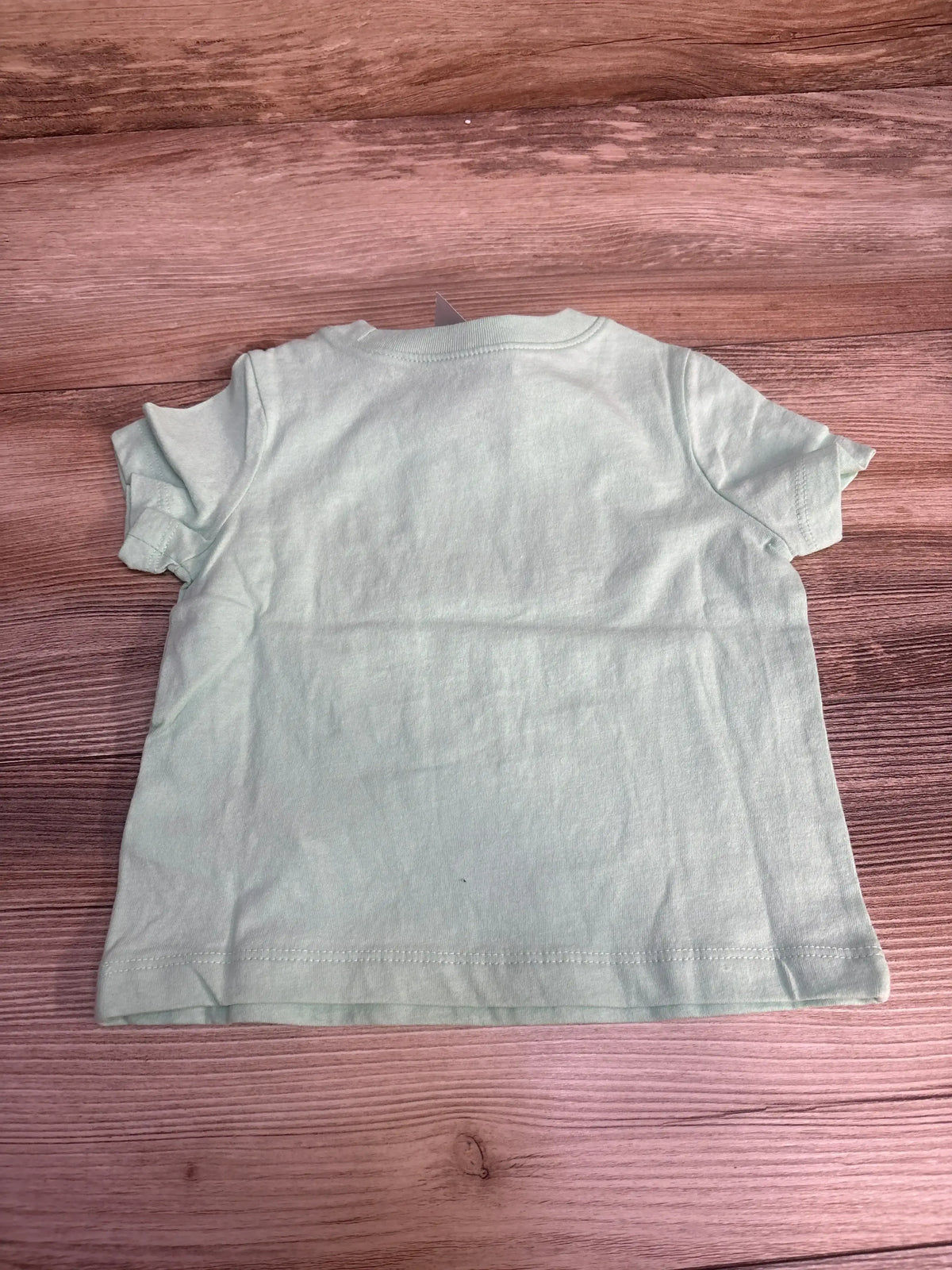 Back view of green Baby Gap short-sleeve baby t-shirt showcasing plain back and crew neckline on wood surface