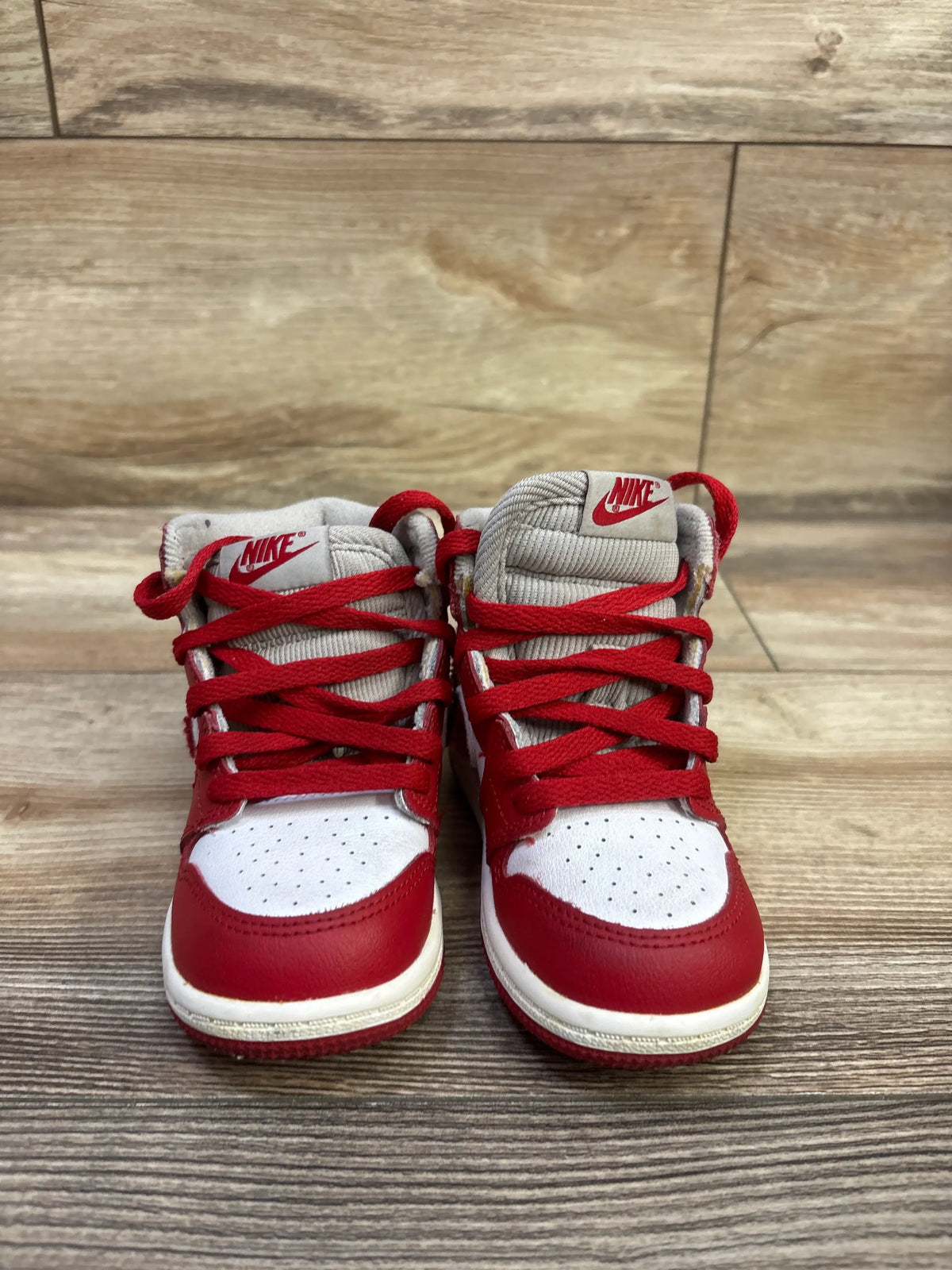 Front view of Air Jordan 1 Retro High OG TD Newstalgia Chenille sneakers with red laces and white toe boxes on wood floor
