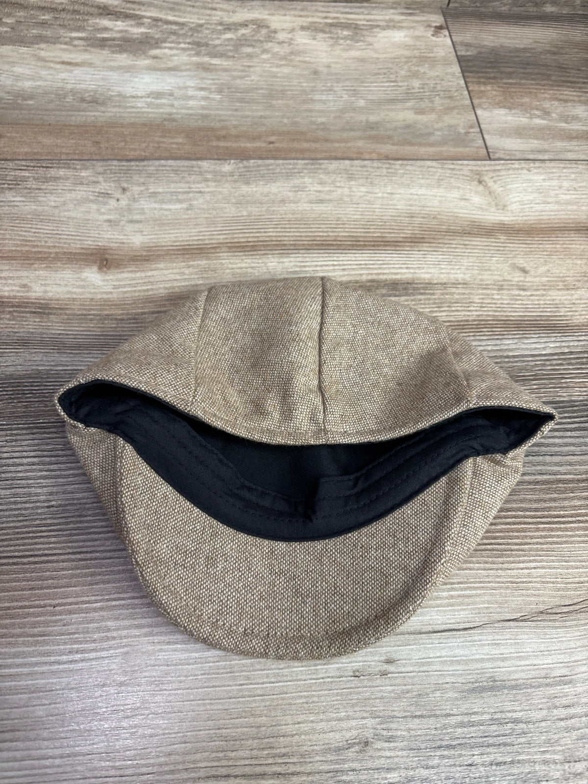 Underside view of Jangoul kids newsboy tweed flat cap in tan, showcasing black lining on a wood-grain background