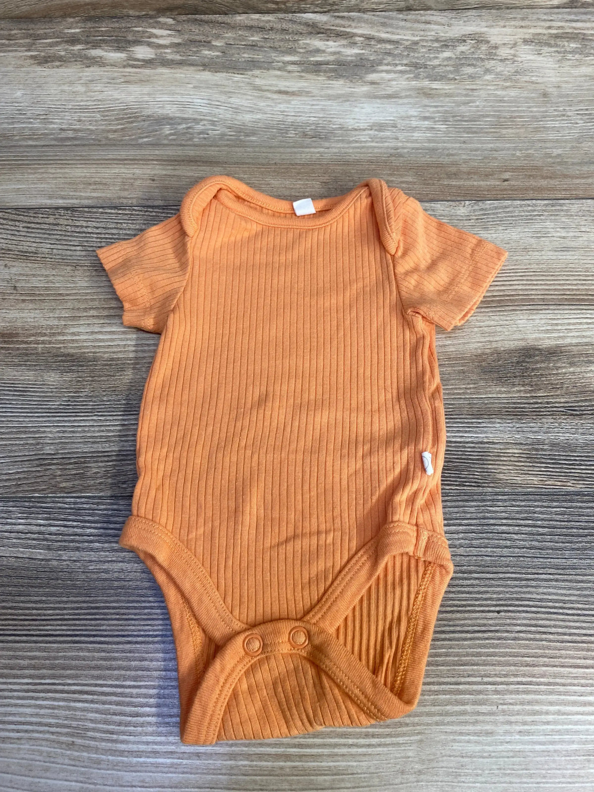 Flat lay of newborn orange ribbed baby bodysuit showcasing short sleeves, snap crotch, and vertical ribbing on light wood background