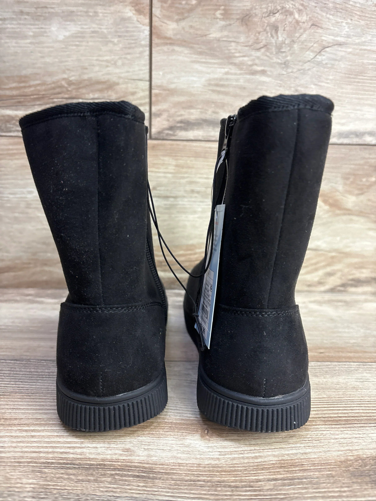 Rear view of Cat and Jack Holland shearling-style black kids boots with rubber soles, back zipper, and tag on wood floor