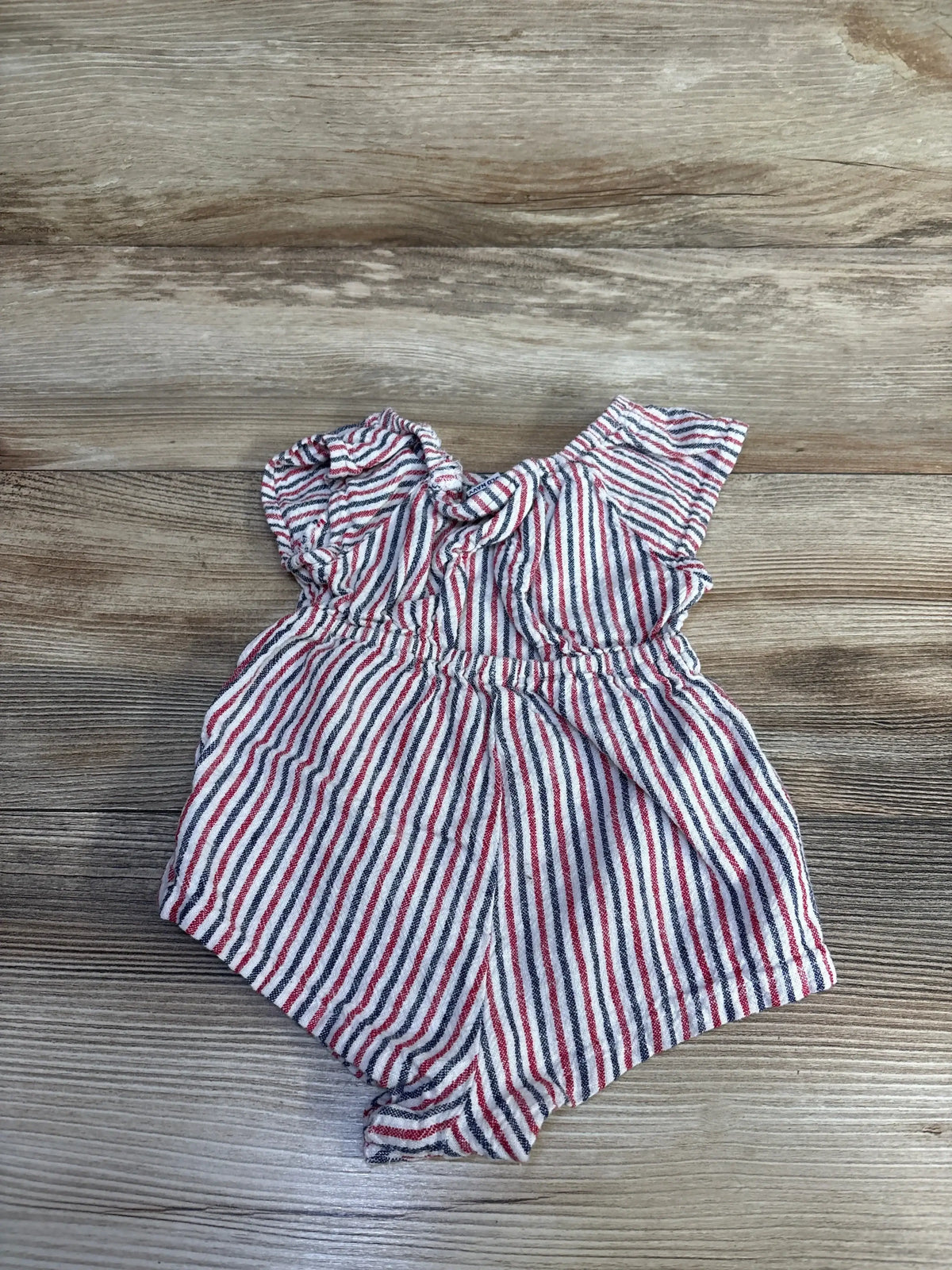 Top-down view of red, white, and navy striped Old Navy linen-blend baby romper with flutter sleeves and elastic waist on wood background