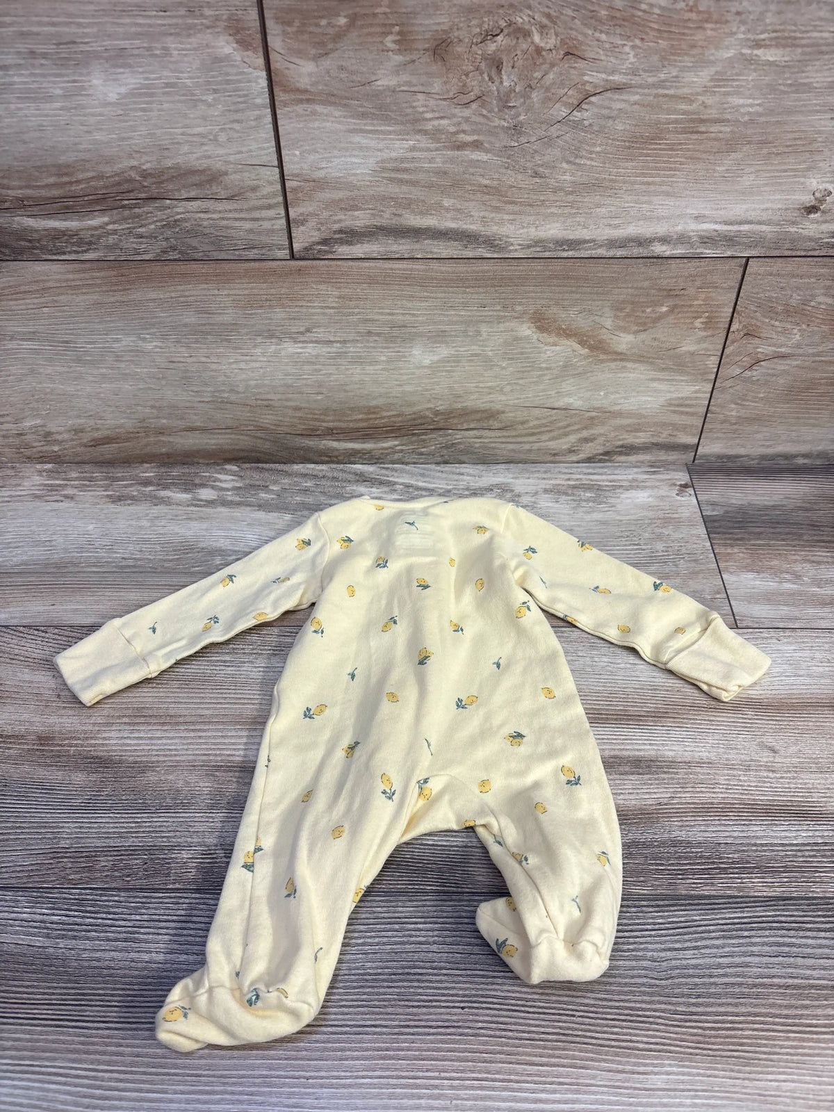 Top view of Carter’s yellow newborn sleeper showcasing long sleeves, footed legs, and fruit print on a wood background