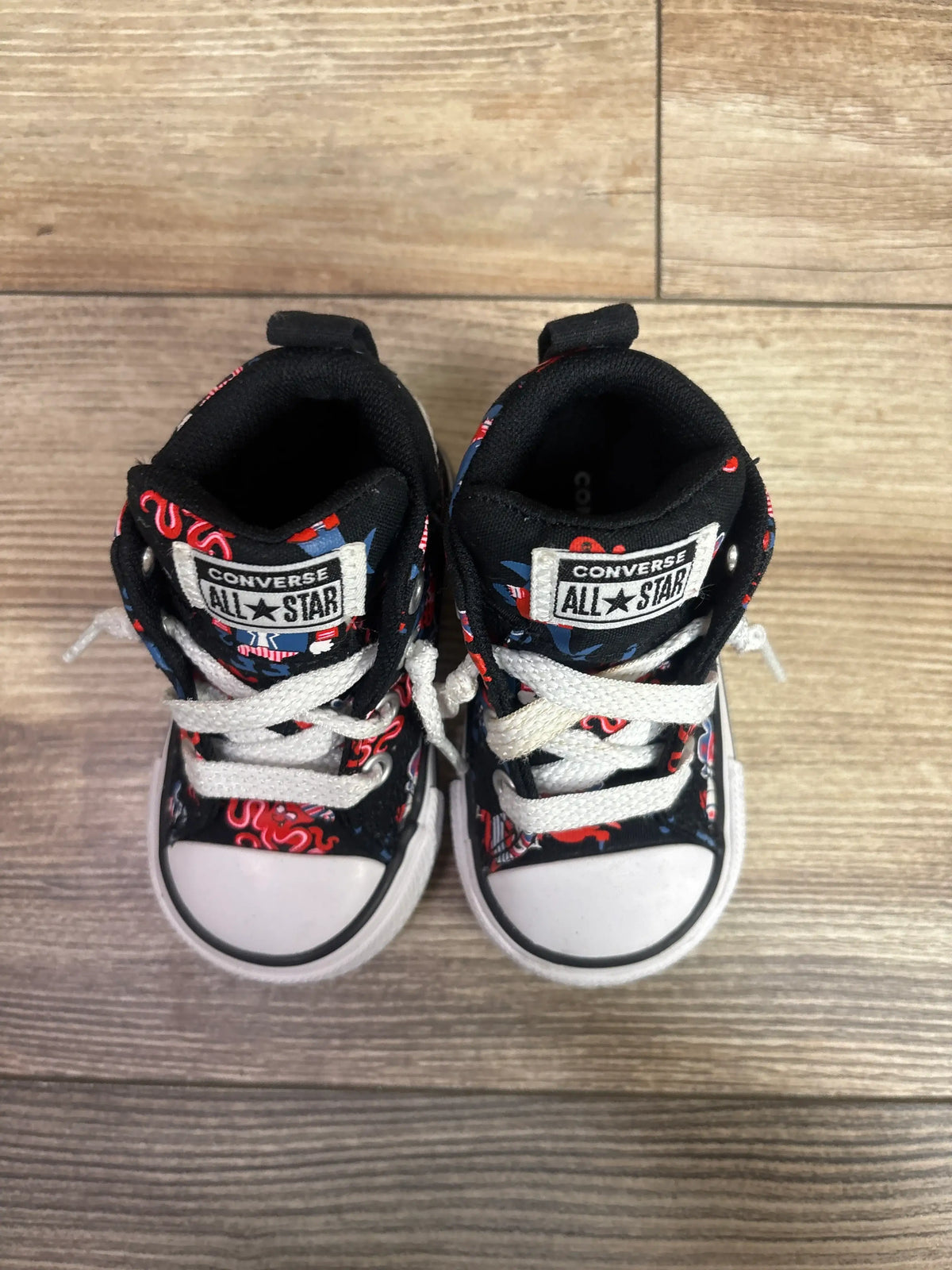Top view of black Converse Chuck All Star Street Mid sneakers with red-blue graphics and white laces on wood floor