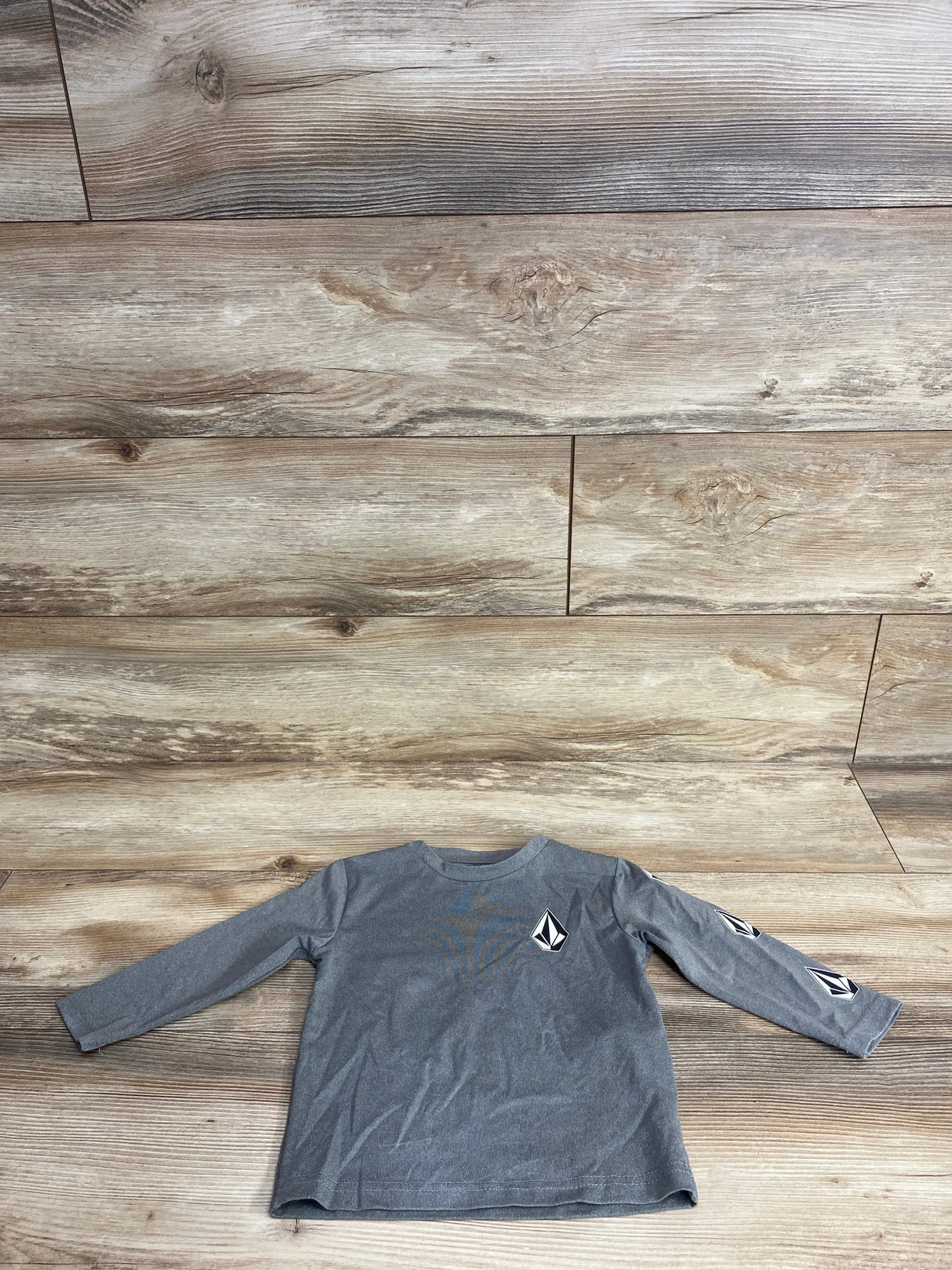 Front view of grey Volcom toddler long-sleeve shirt (2T) showing black-and-white diamond logo on chest and sleeve on wood floor background
