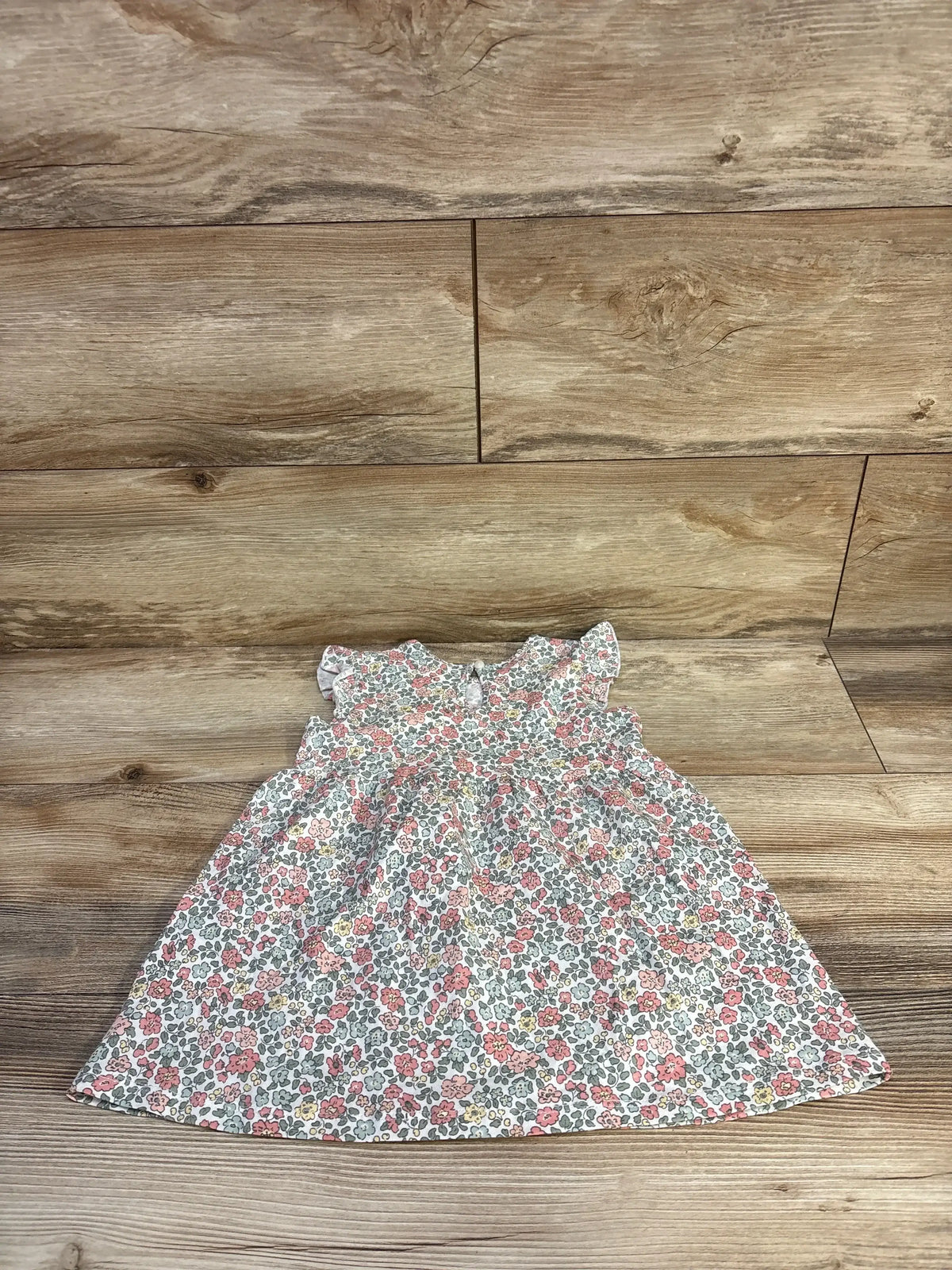 Front view of H&M white cotton dress, size 18m, with pink and yellow floral print and ruffled cap sleeves on wood background