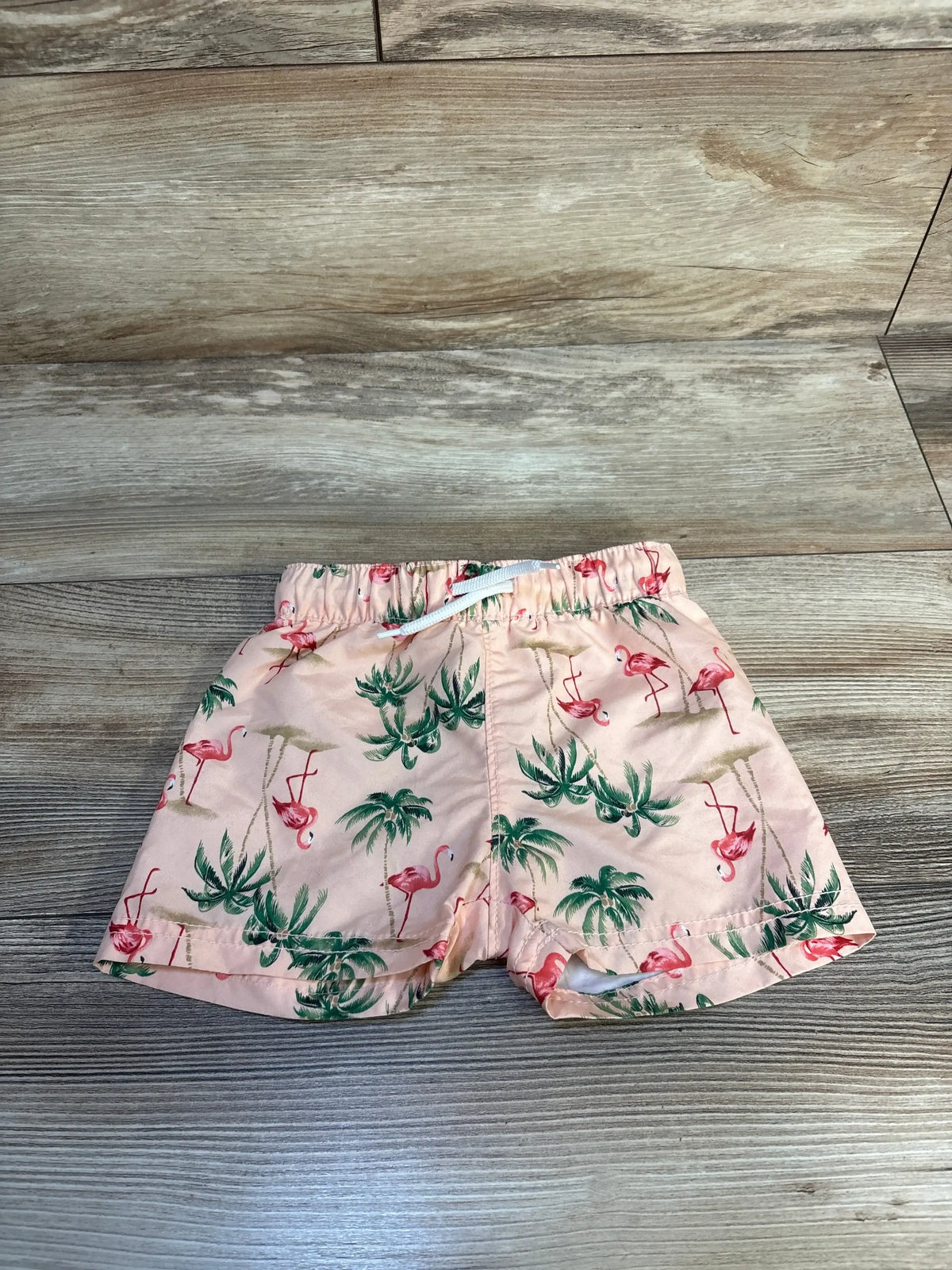 Pink toddler shorts with green palm tree and flamingo print on wooden floor