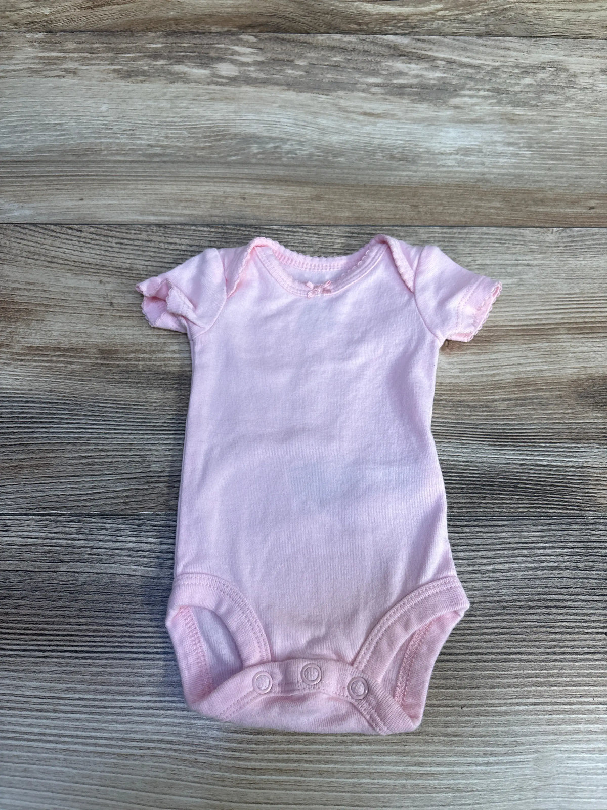Front view of Simple Joys pink short-sleeve bodysuit showcasing snap closures with a wood-grain background