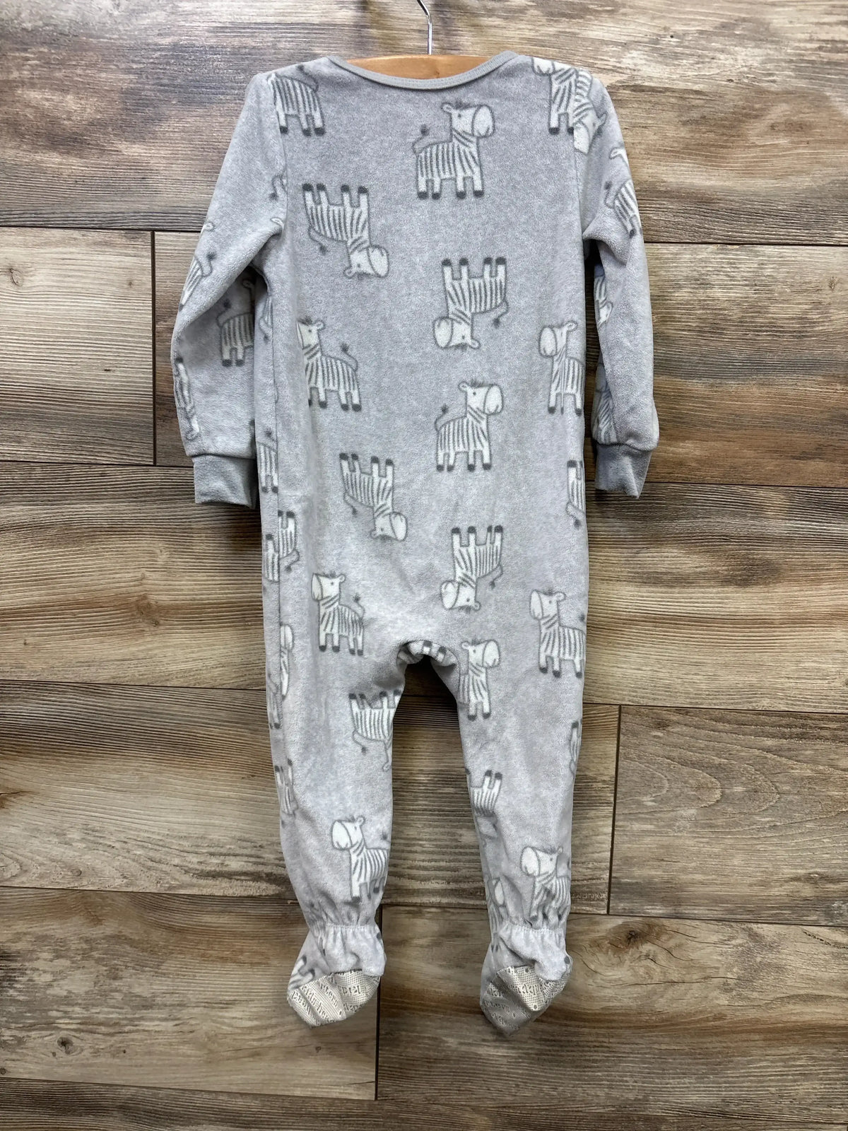 Gray baby onesie with zebra print, long sleeves, footed design, hanging on hanger against wood background