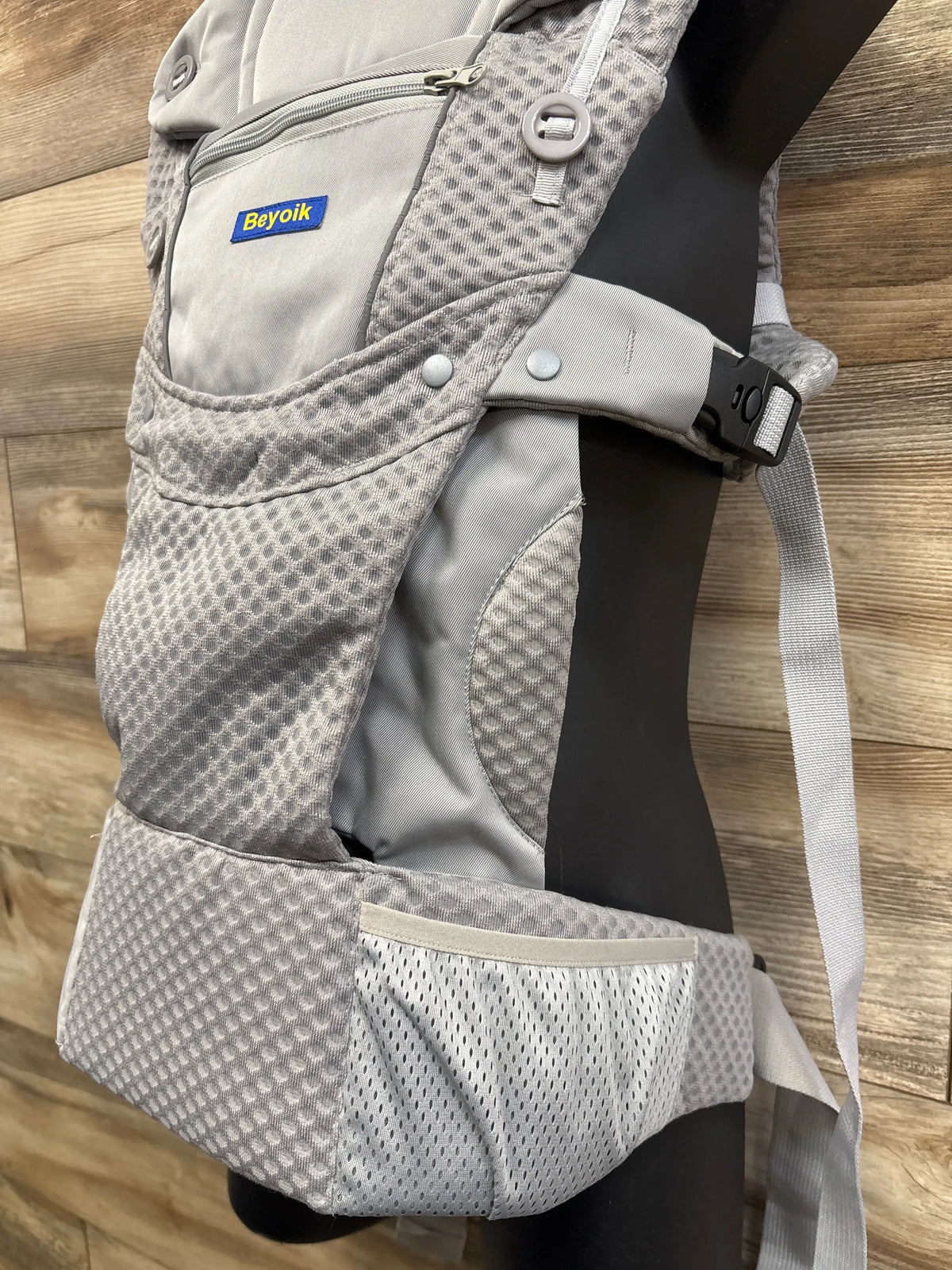 Close-up of grey Beyoik all-position baby carrier with breathable mesh panels, buckles, and padded straps on a wood floor