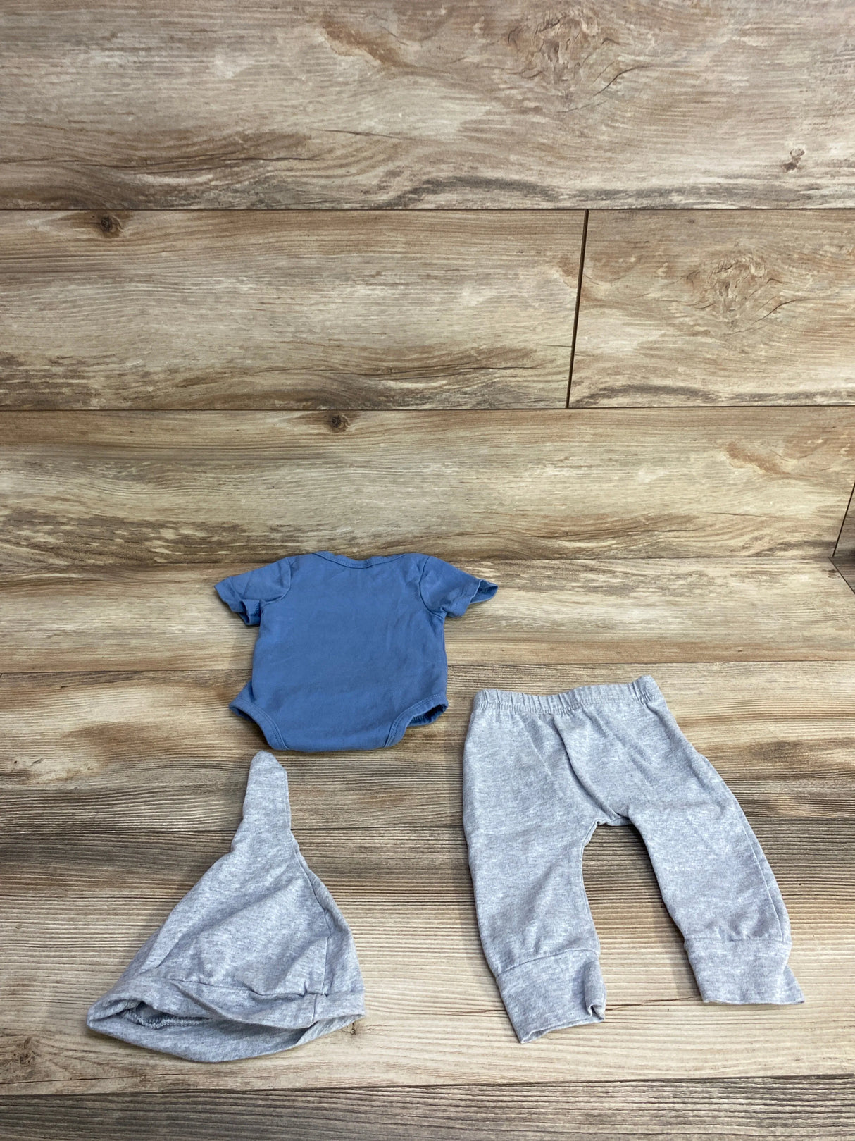 Blue baby onesie, gray baby hat, and gray baby pants on wooden background for kids clothes resale