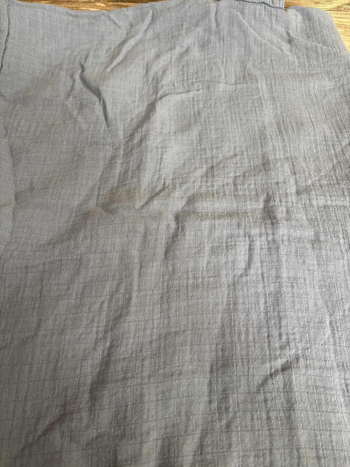 Flat lay of Comfy Cubs muslin car seat cover showcasing light blue soft crinkled fabric with subtle grid texture on wooden surface
