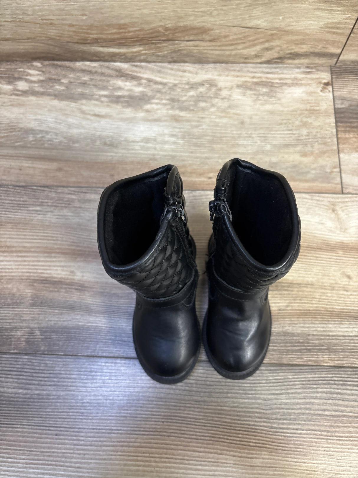 Top view of Carter’s black quilted toddler riding boots showing quilted shaft and side zippers on wood floor