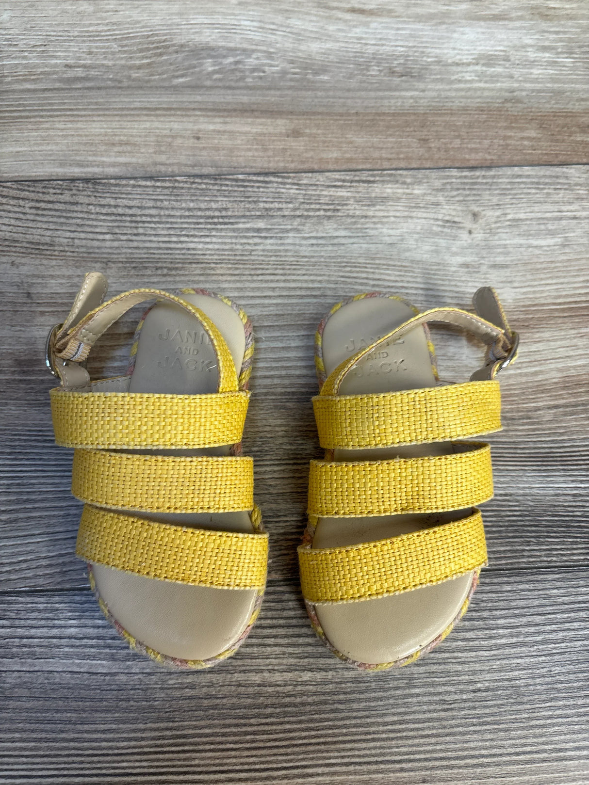 Yellow woven toddler sandals with ankle straps on wood background