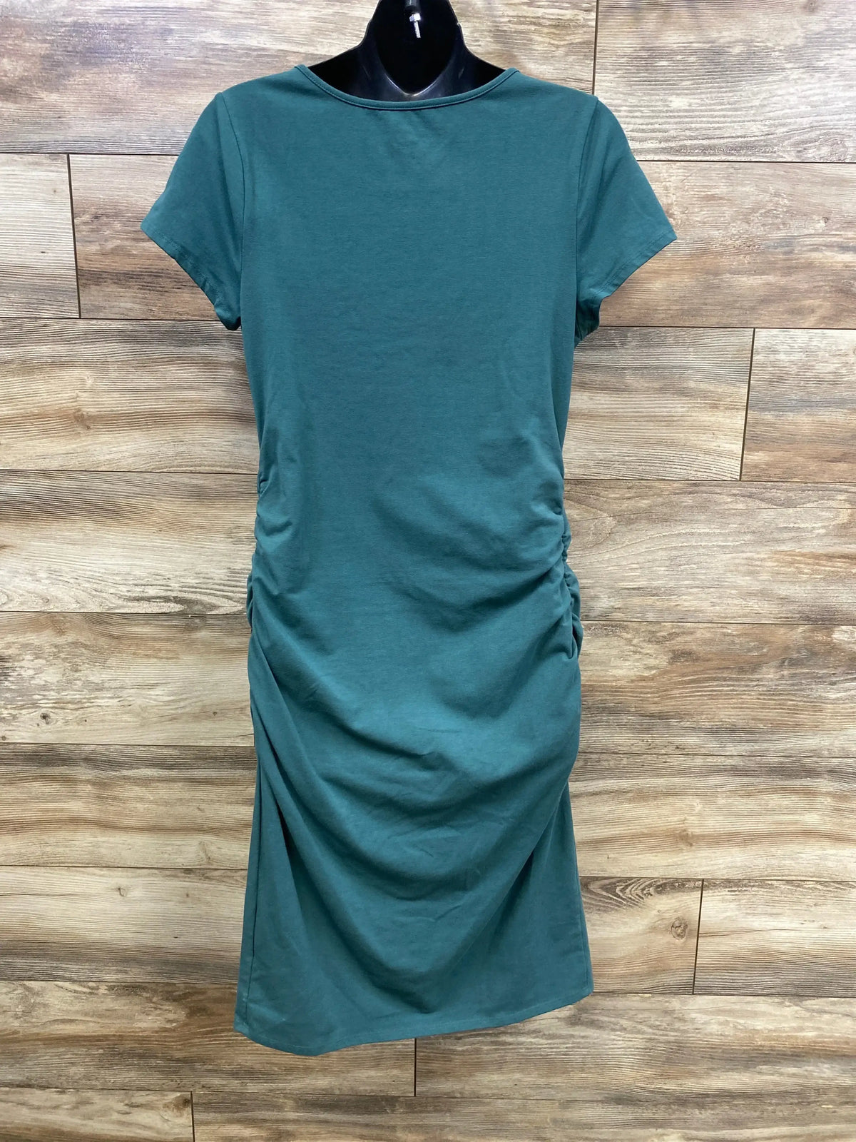 Front of Isabel maternity green bodycon dress with side ruching and short sleeves on black mannequin, wood background