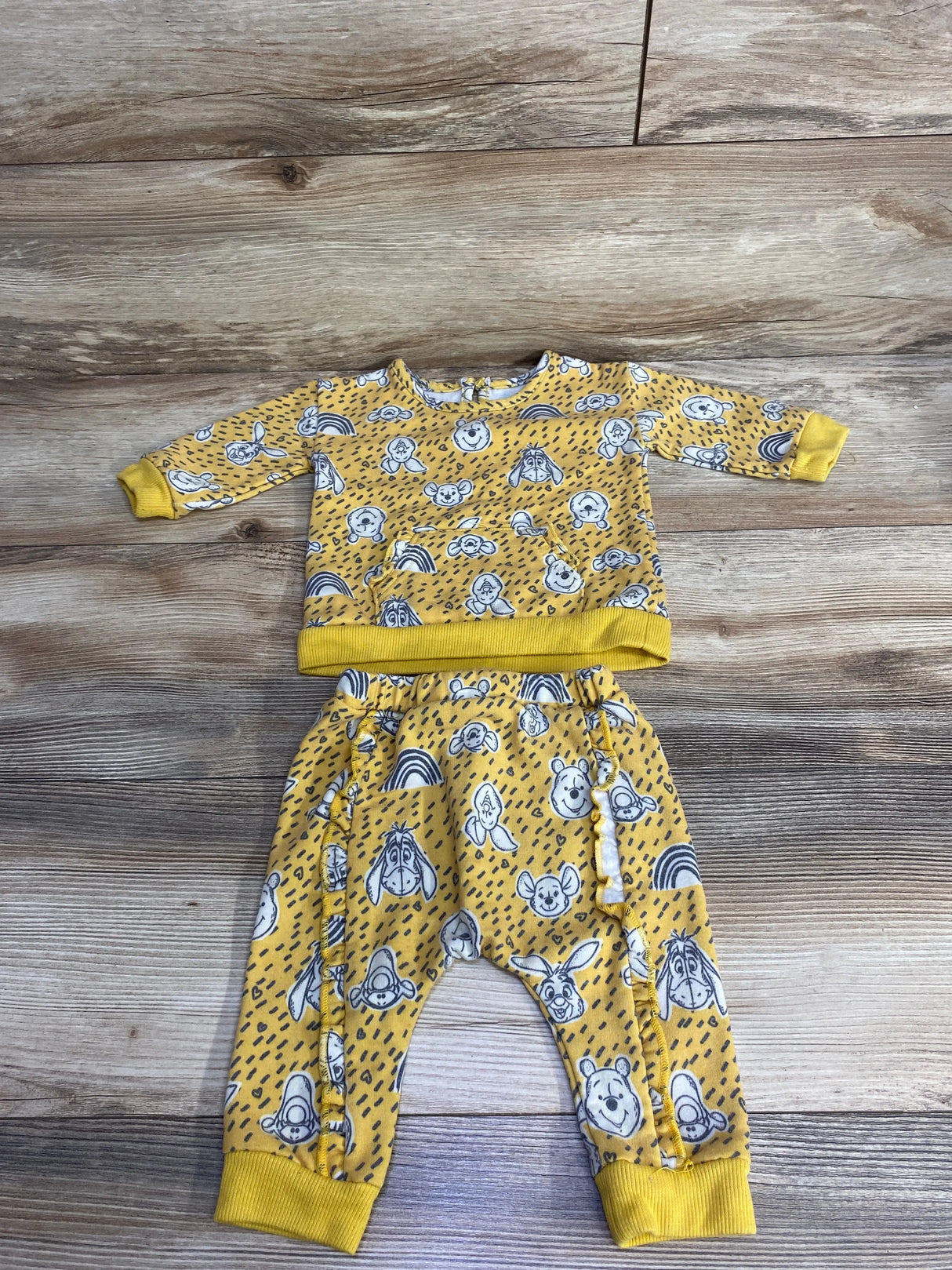 Yellow toddler outfit with Winnie the Pooh and friends print, featuring long-sleeve top and pants on wooden surface